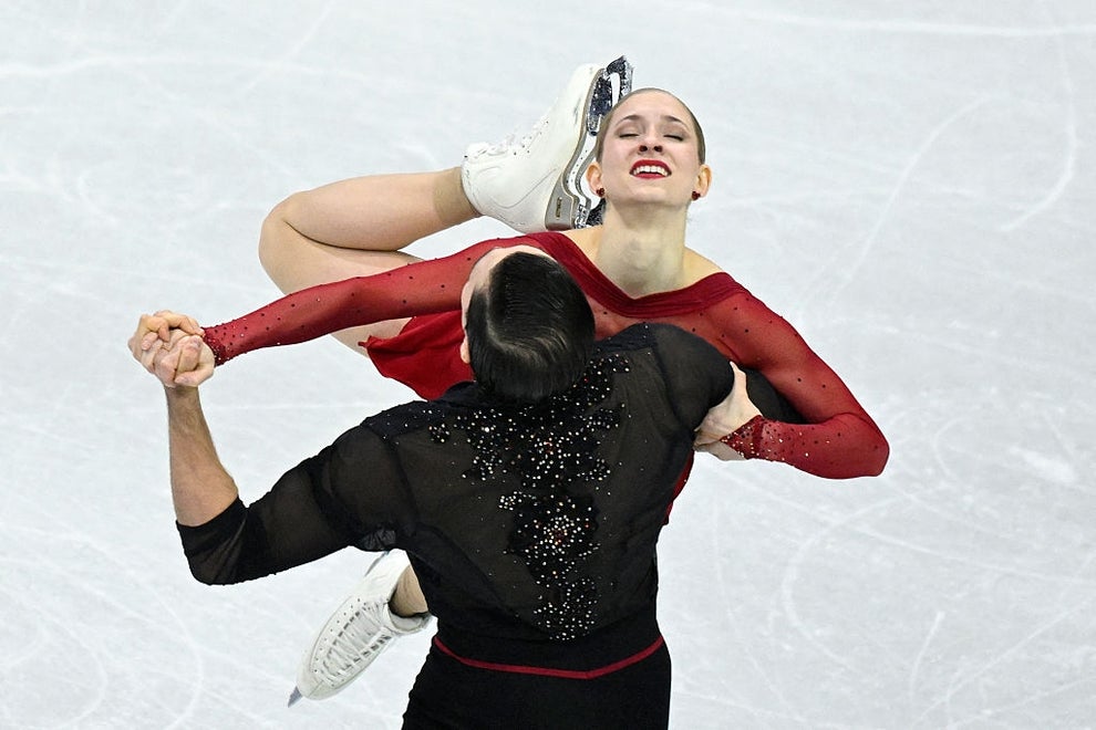 Figure skating duo mid-performance, with one skater lifting the other gracefully, wearing elegant, sparkling outfits on the ice