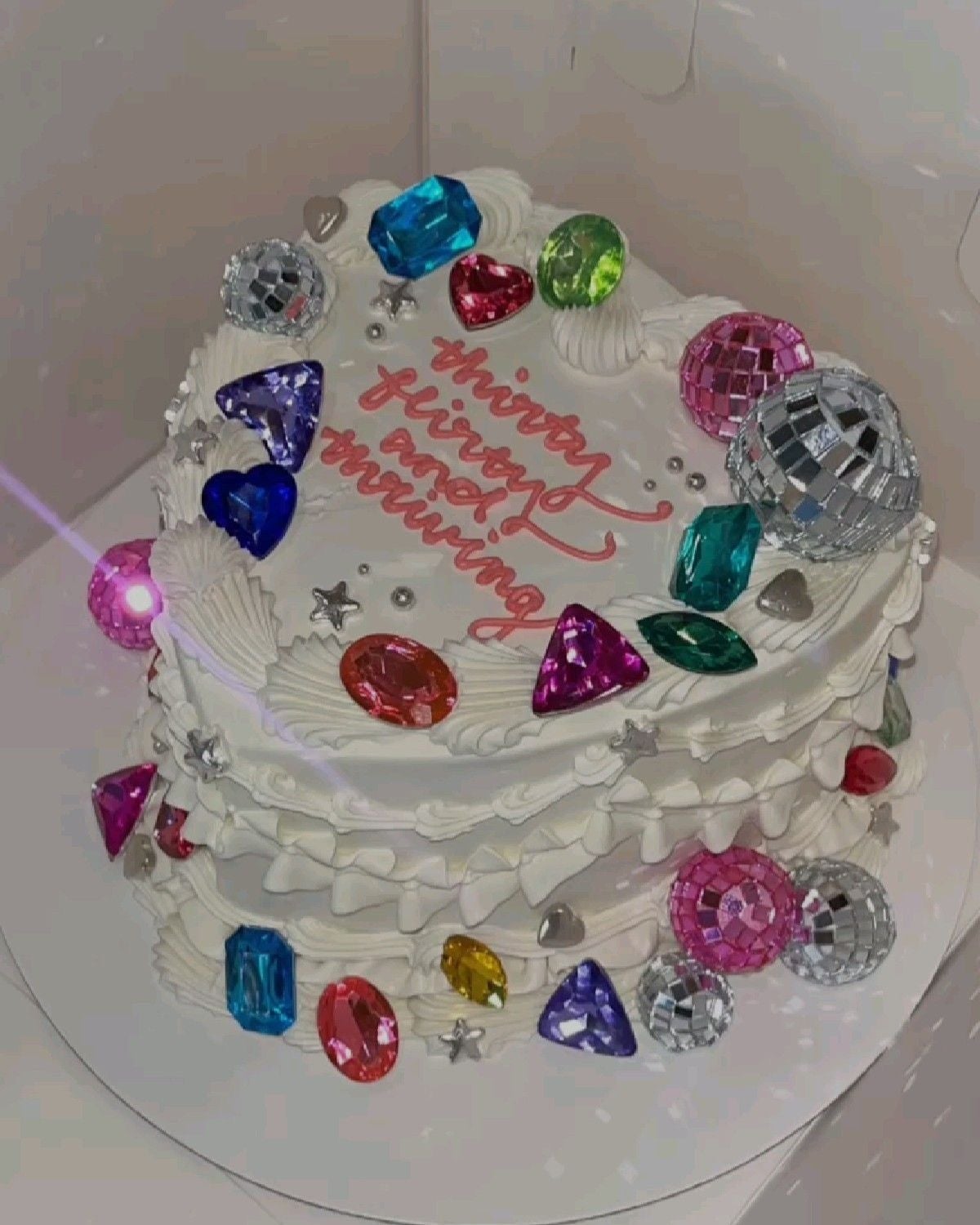 Pastel en forma de corazón decorado con joyas falsas y texto en la parte superior: "thirty, flirty, and thriving"