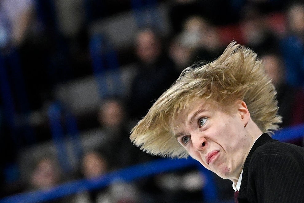 Person ice skating, with a dynamic expression and hair flying, mid-performance in an arena