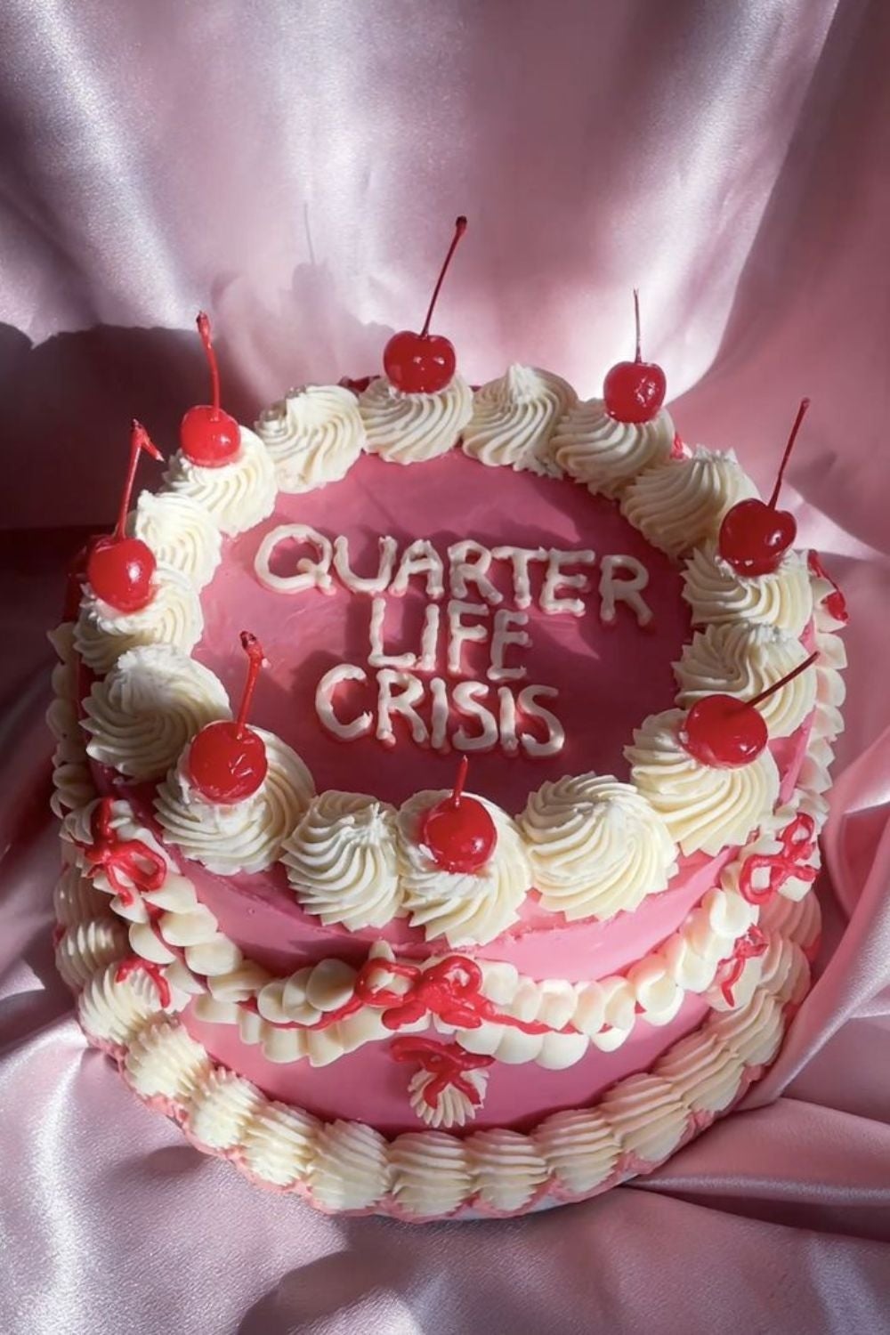 Pastel con cerezas y crema, decorado con el texto "QUARTER LIFE CRISIS" sobre una tela satinada