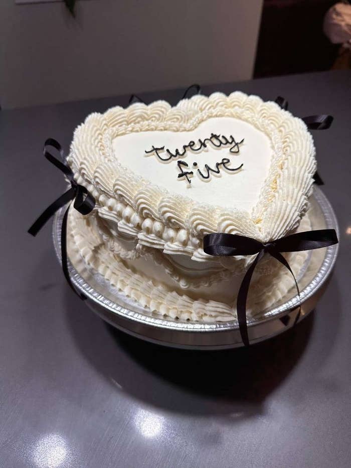 Pastel de corazón con glaseado rizado y lazo negro. Texto en el pastel: "twenty five"