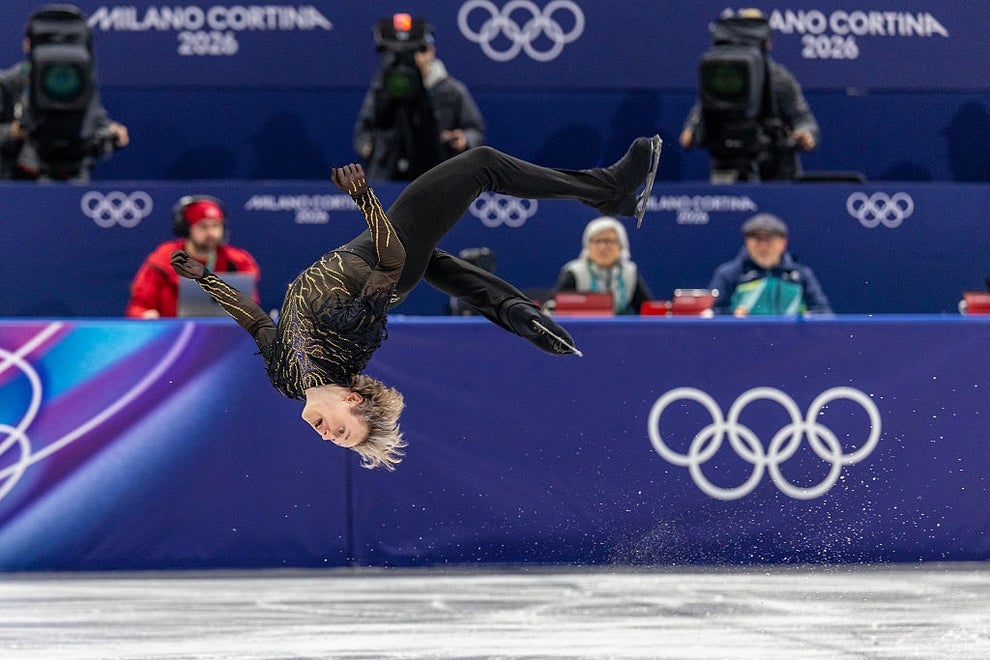 Figure skater performs a mid-air spin during Milano Cortina 2026 Winter Olympics event, wearing a sleek, patterned outfit
