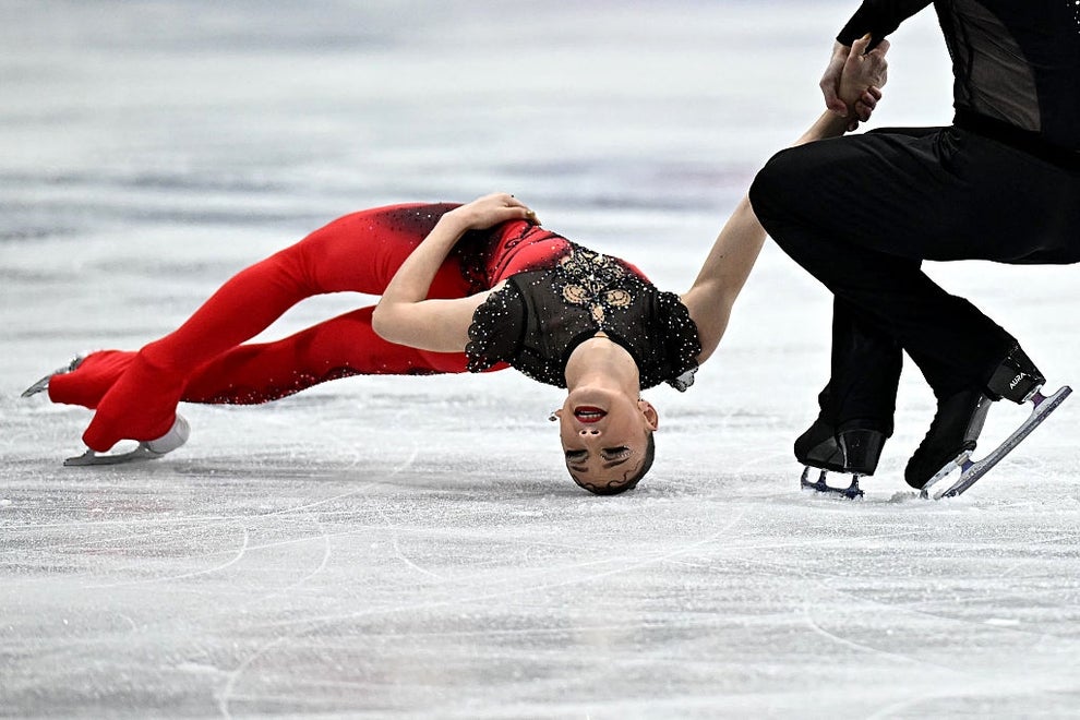 Figure skaters perform an impressive move on the ice, with one skater bending backward while holding hands with a partner in a dynamic pose