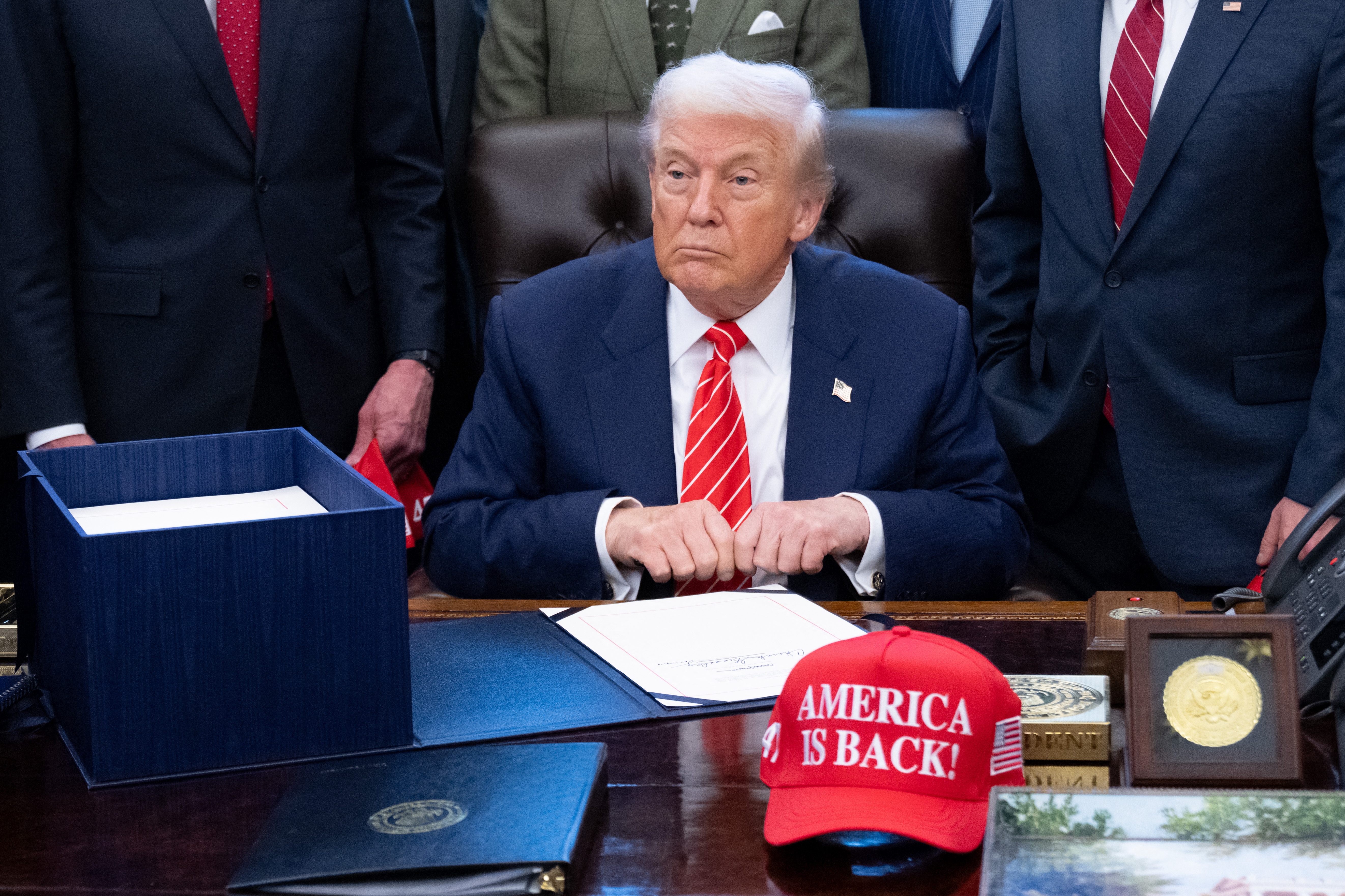 A idiosyncratic   astatine  a table  with an "America is Back!" hat, surrounded by documents and others successful  suits