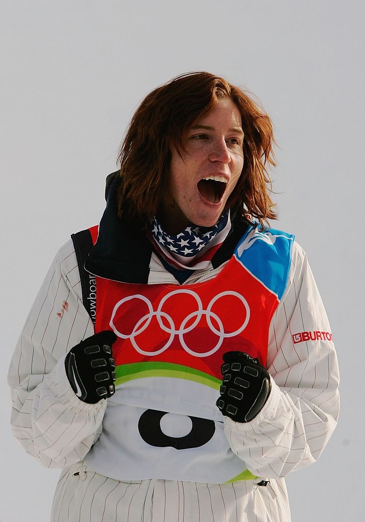 Person successful Olympic snowboarding gear, cheering with excitement. They deterioration a patterned cervix scarf and a reddish bib with the Olympic rings