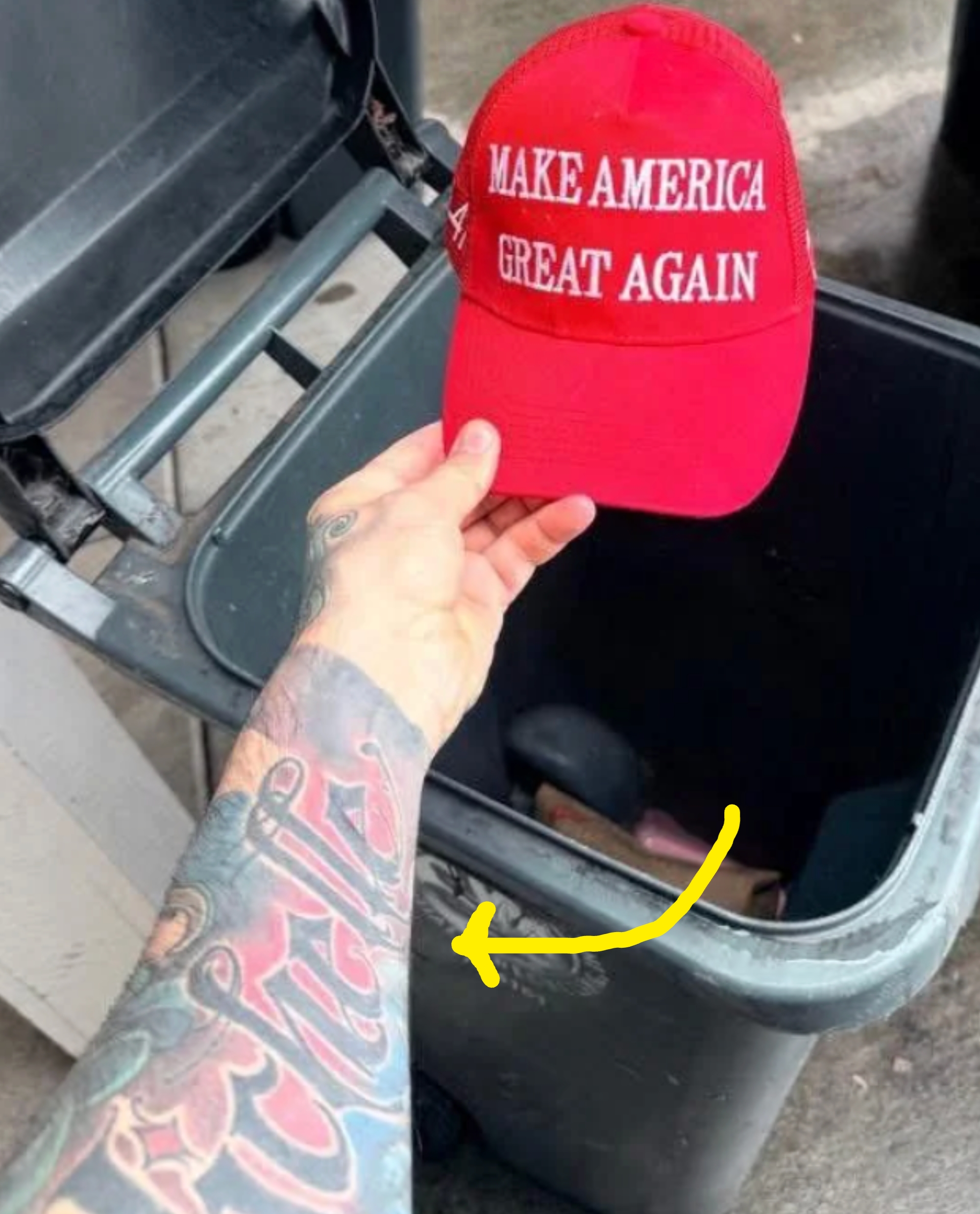A tattooed limb  holds a "Make America Great Again" headdress  supra  a trash can, extracurricular  adjacent   different   bins