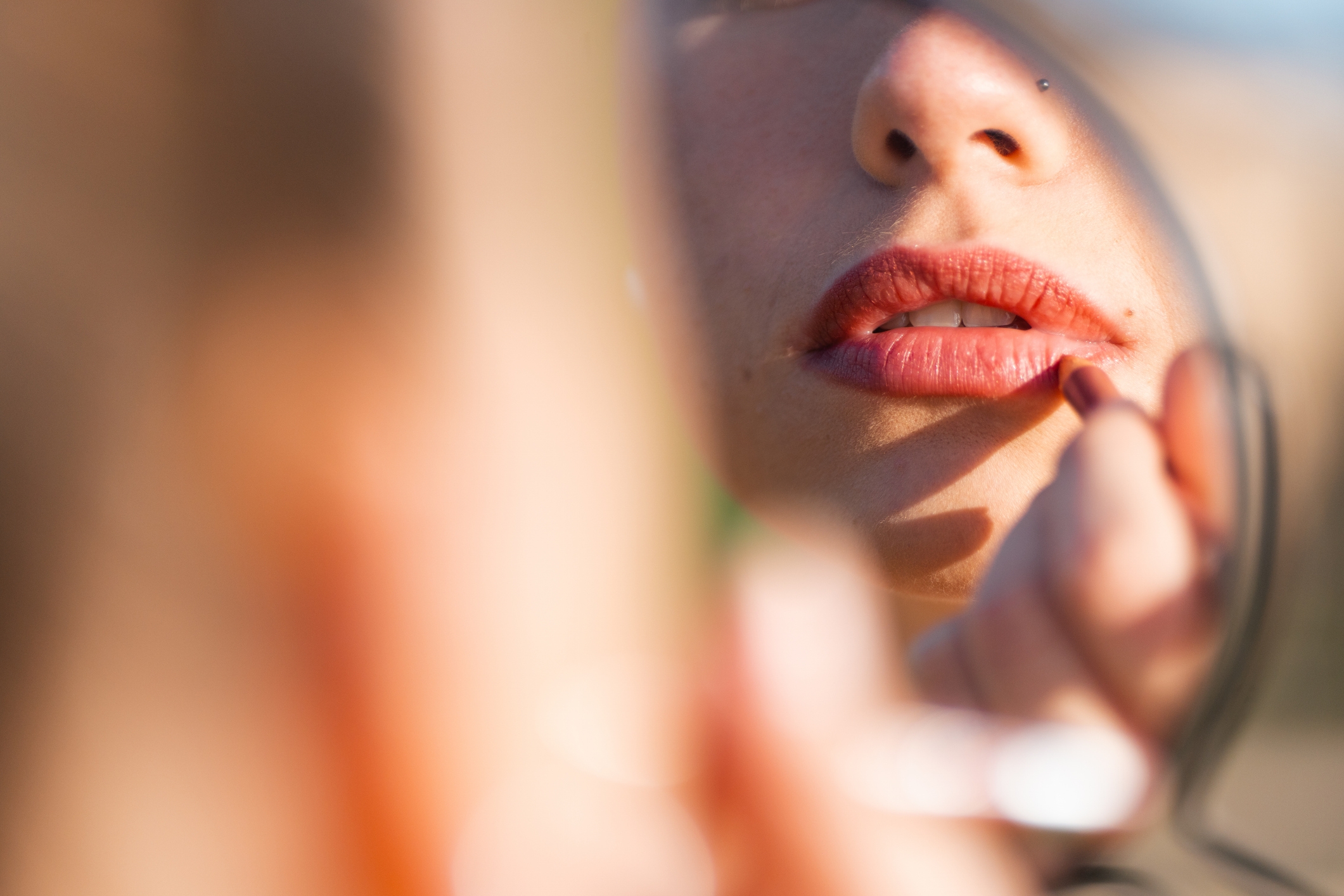 Partial reflection of a idiosyncratic applying lipstick, focusing connected their lips and the reflector they are using