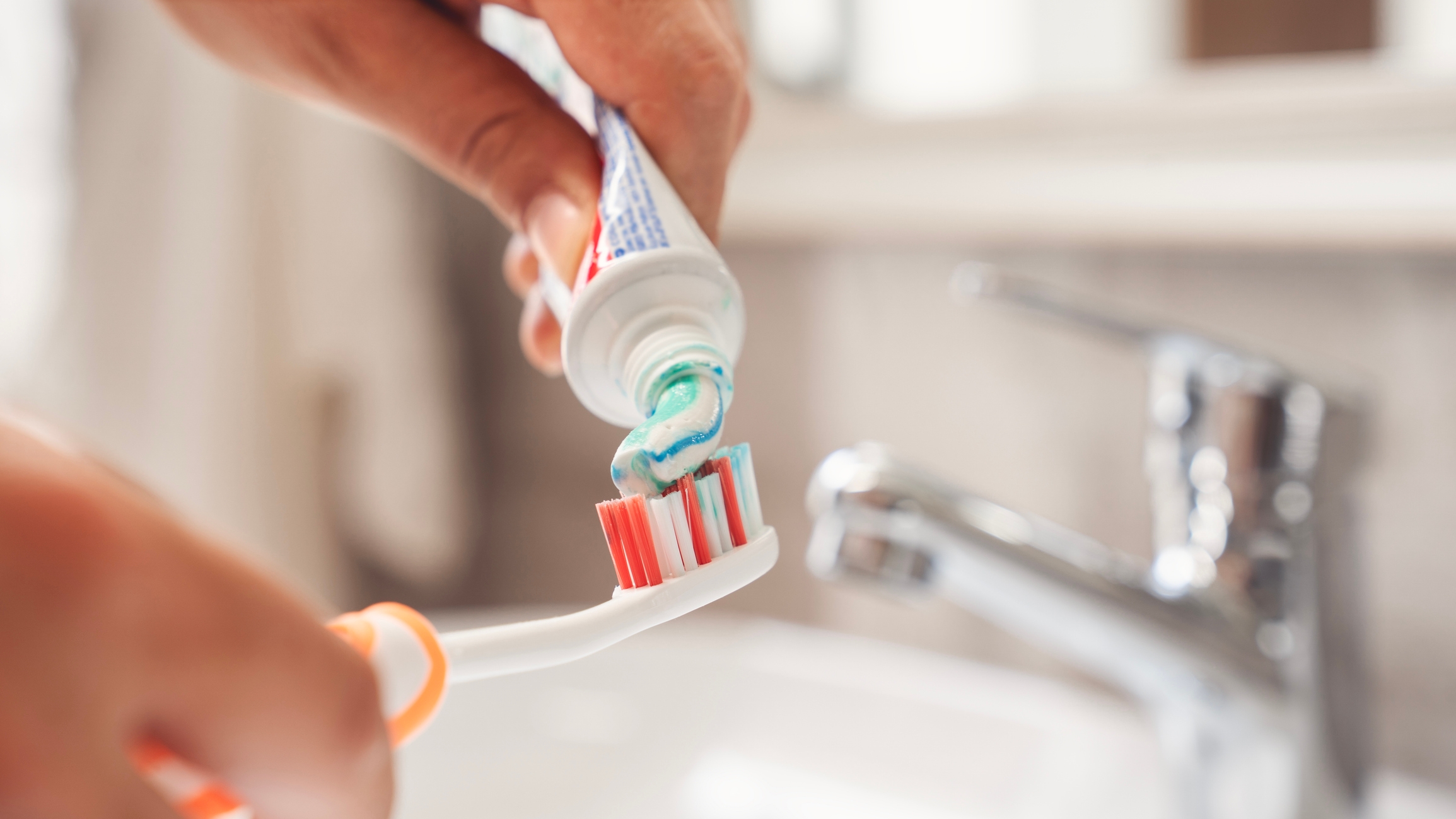 A manus squeezes toothpaste onto a toothbrush implicit a bath sink, preparing for brushing teeth