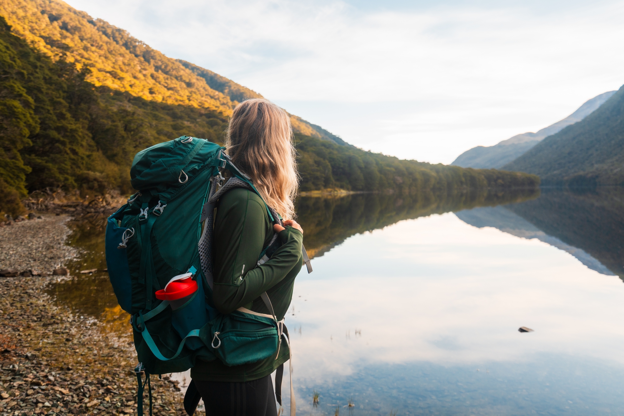 Person with a backpack gazes astatine a peaceful lakeside, surrounded by mountains and trees