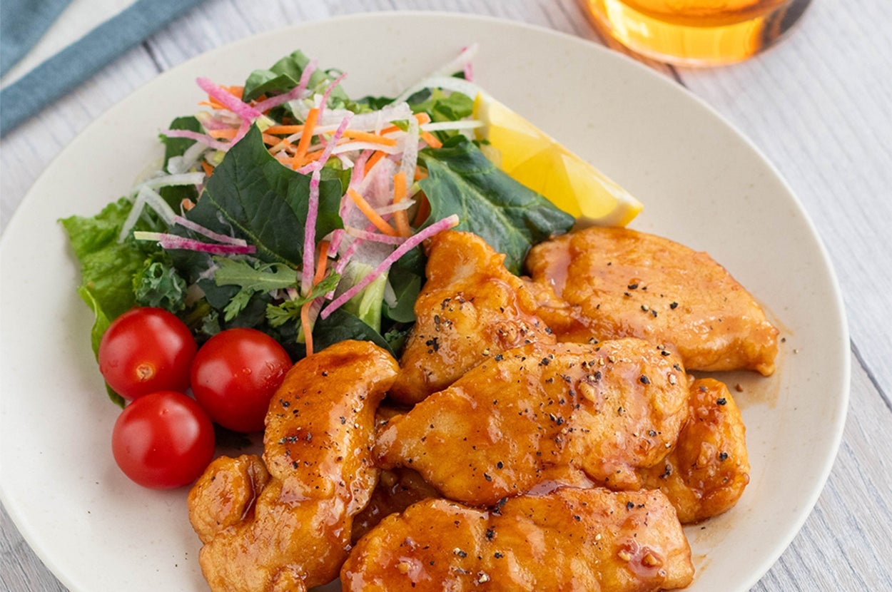 皿の上に盛られた鶏肉とサラダ、トマト、レモンのくし形切り。右上に飲み物のグラス。