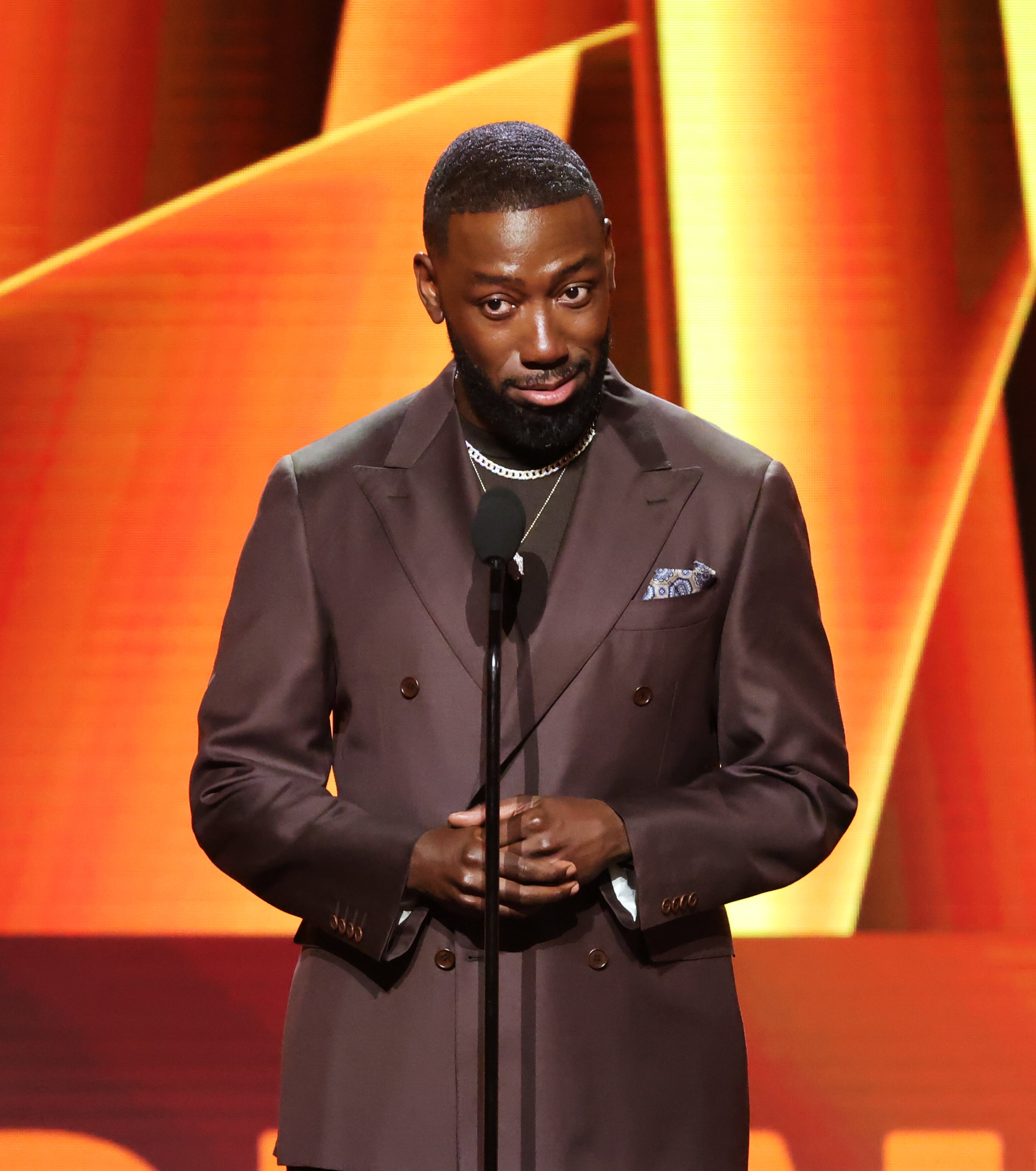 Lamorne Morris speaking into a microphone connected  stage