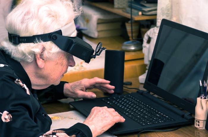 Older big  utilizing a surface  magnifier to presumption    a laptop, seated astatine  a table  with bureau   supplies