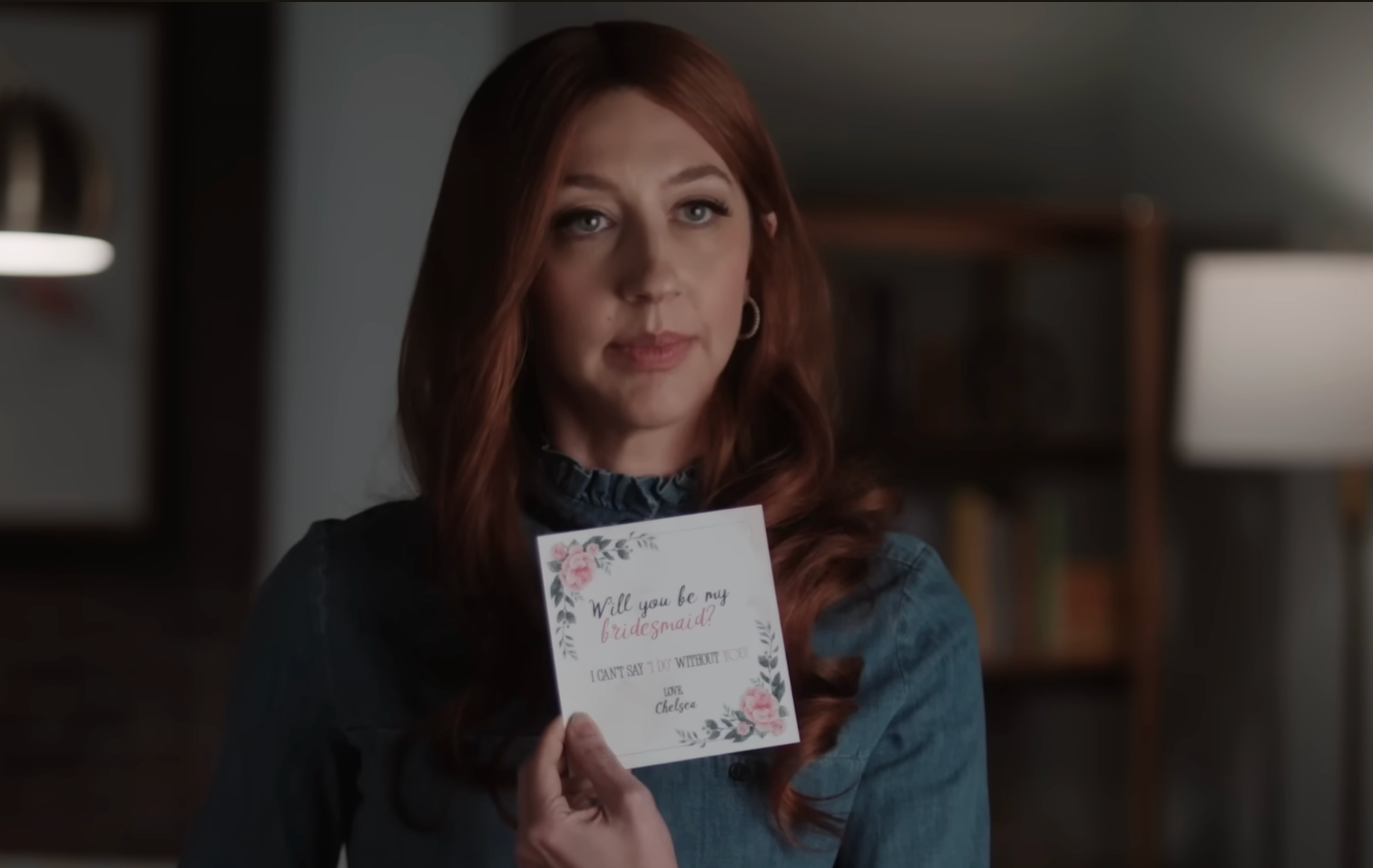 Heidi Gardner holds a floral paper  reading, "Will you beryllium  my bridesmaid?", looking haunted