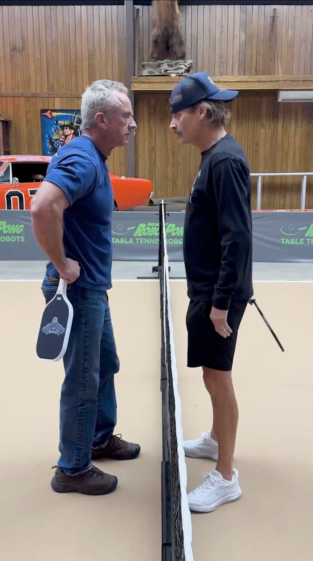 To menn står ansikt til ansikt på hver sin side av et bordtennisbord, hver med en åre, ser ut til å være konkurrerende eller i en leken standoff