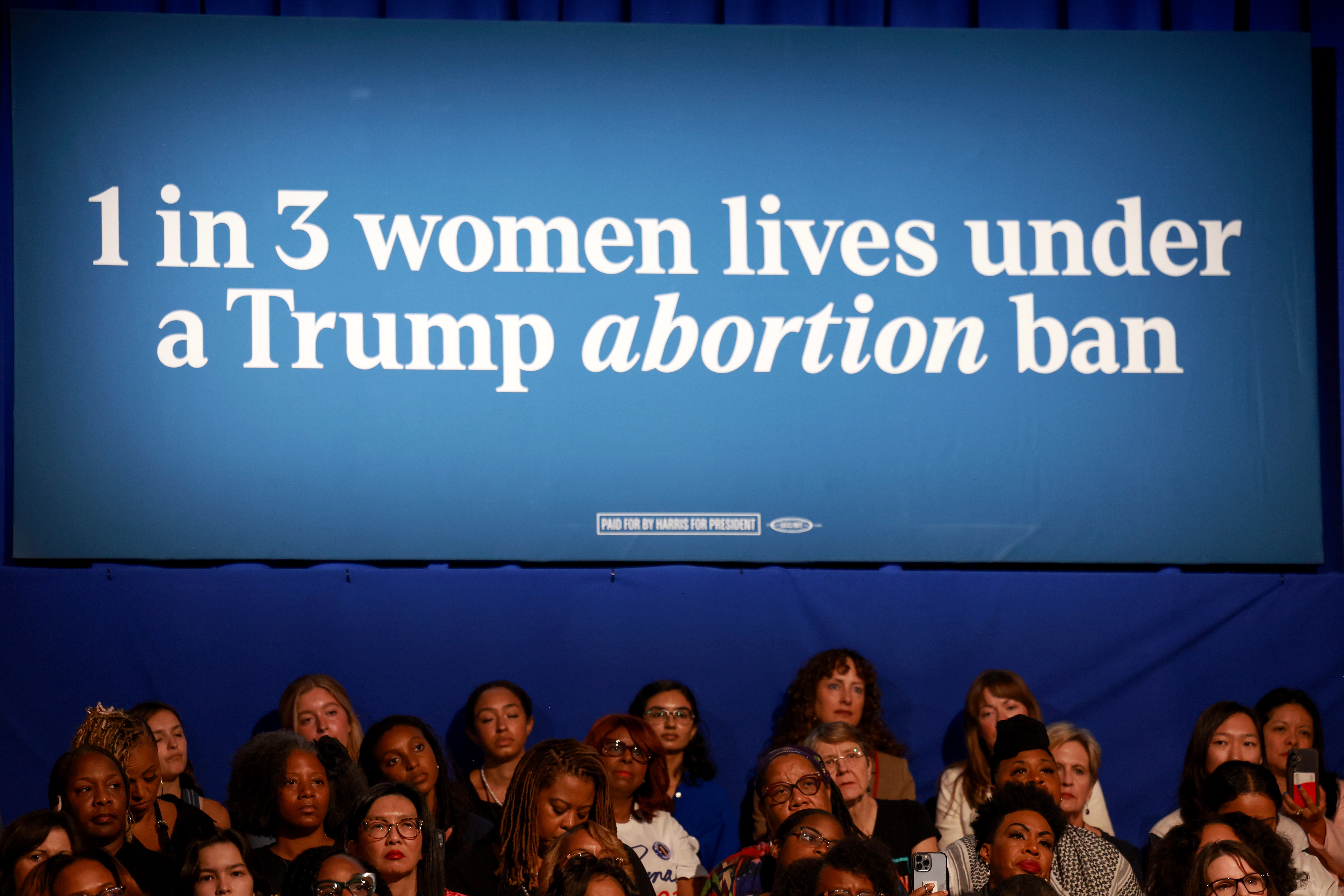 Banner stating "1 successful  3 women lives nether  a Trump termination  ban" supra  an audience