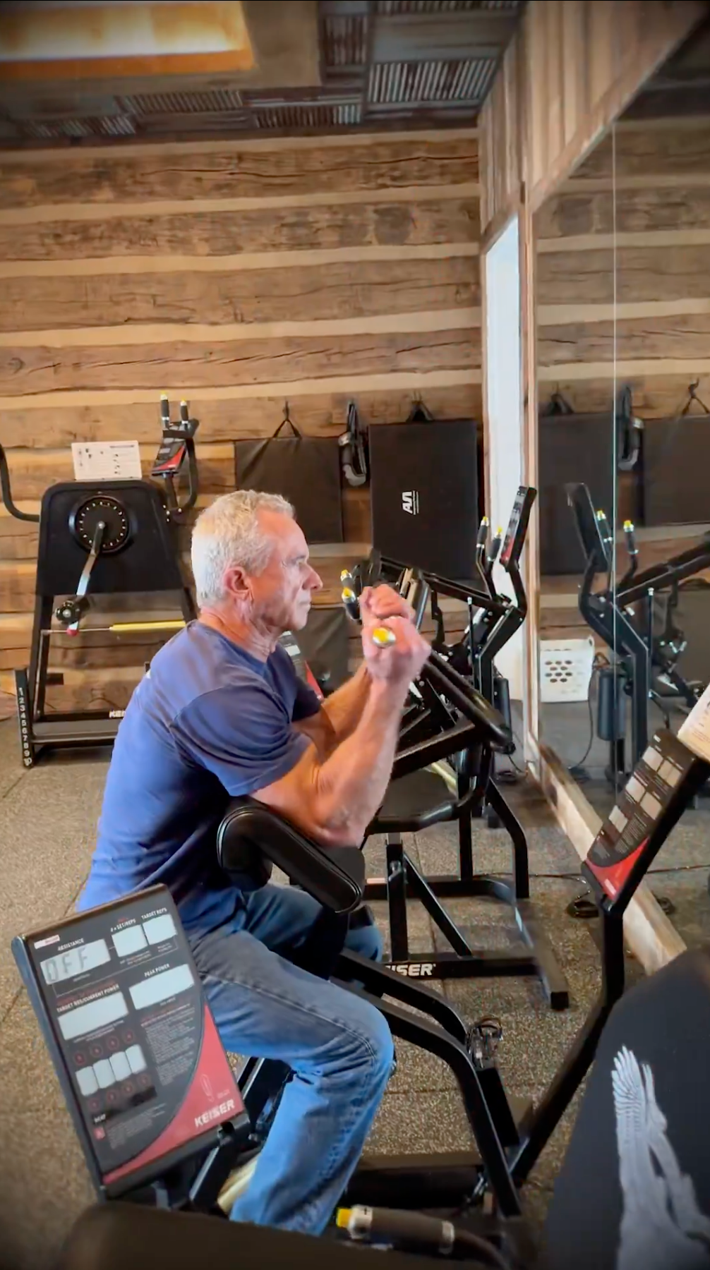 En person trener på en romaskin i et treningsstudio, med fokus på treningen. Refleksjoner er synlige i speilet