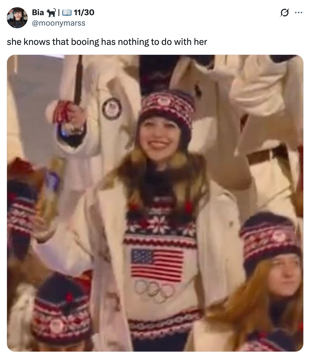 En person i patriotisk vinterantrekk med olympiske symboler smiler, omgitt av andre i lignende antrekk. Bildetekstvitser om å ignorere bop