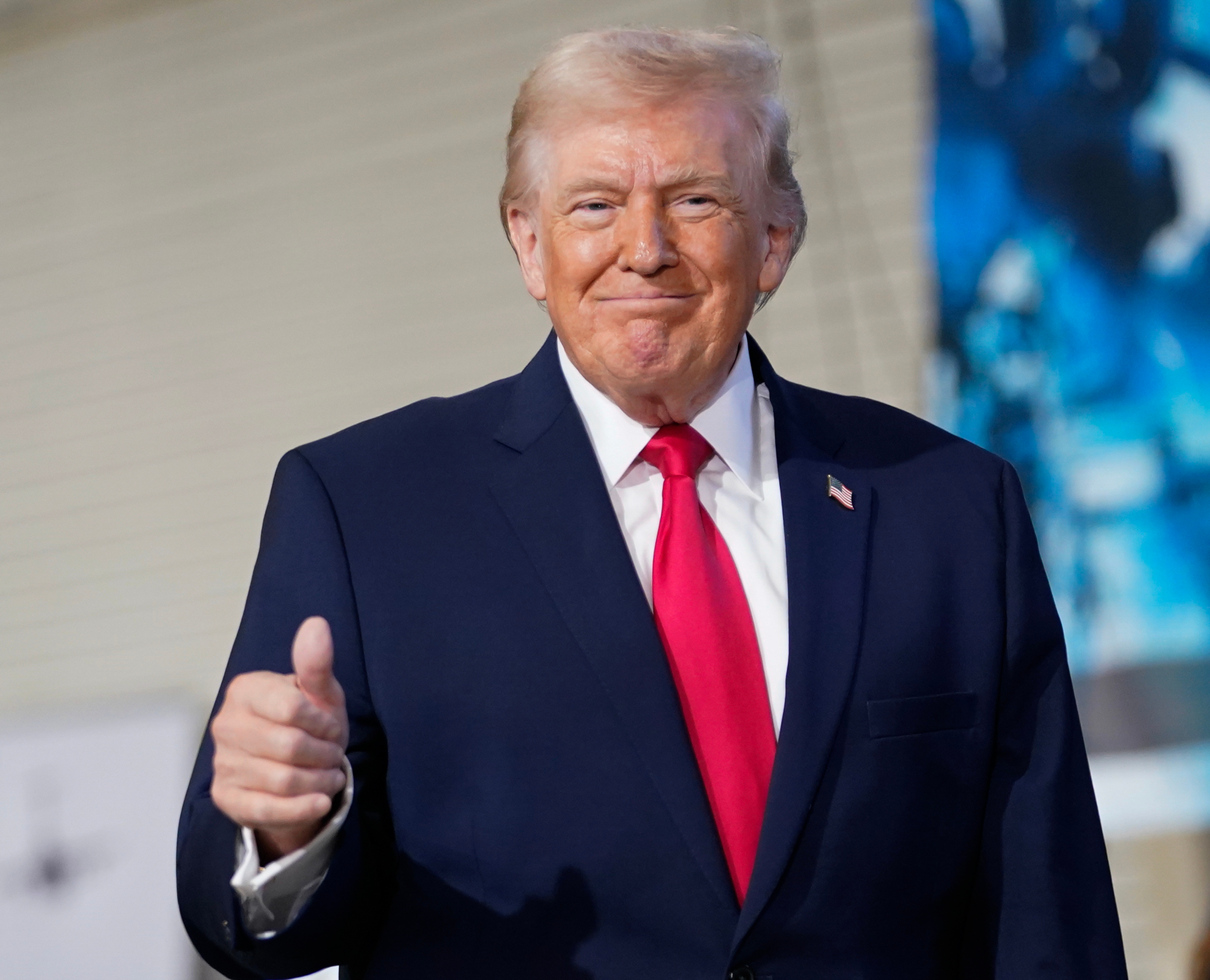 Man successful  a suit   and reddish  necktie  giving a thumbs-up gesture, lasting  indoors with a blurred background