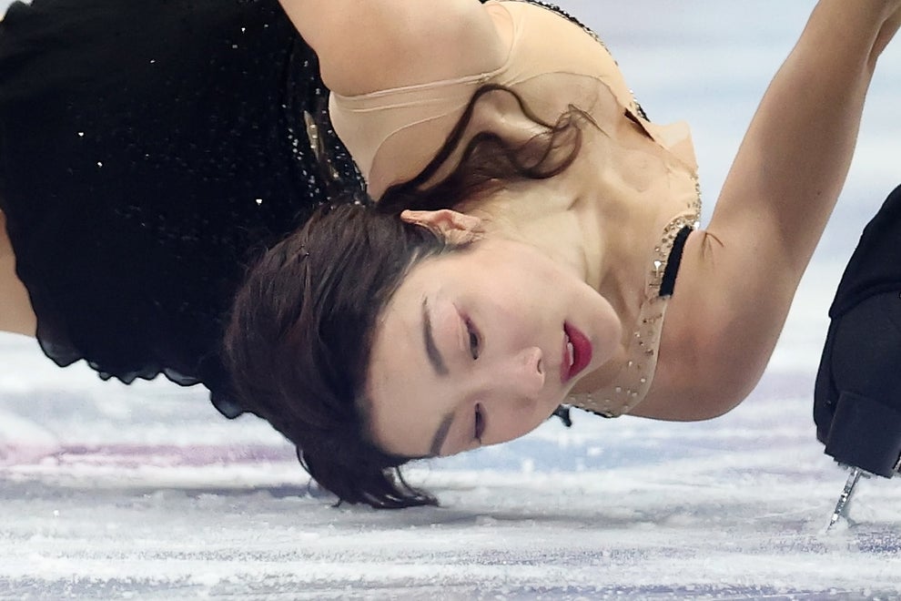 Figure skater in an elegant, sleeveless dress performs a dramatic move on the ice