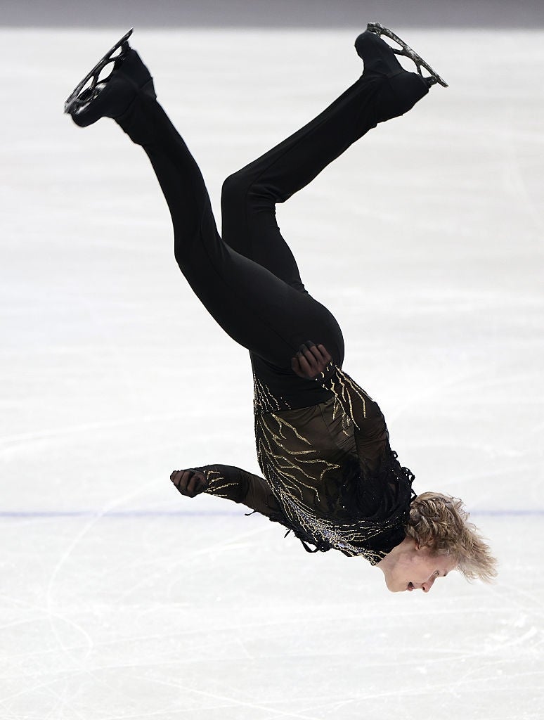 Figure skater mid-air during a jump, wearing a sleek costume with sparkling details, on an ice rink