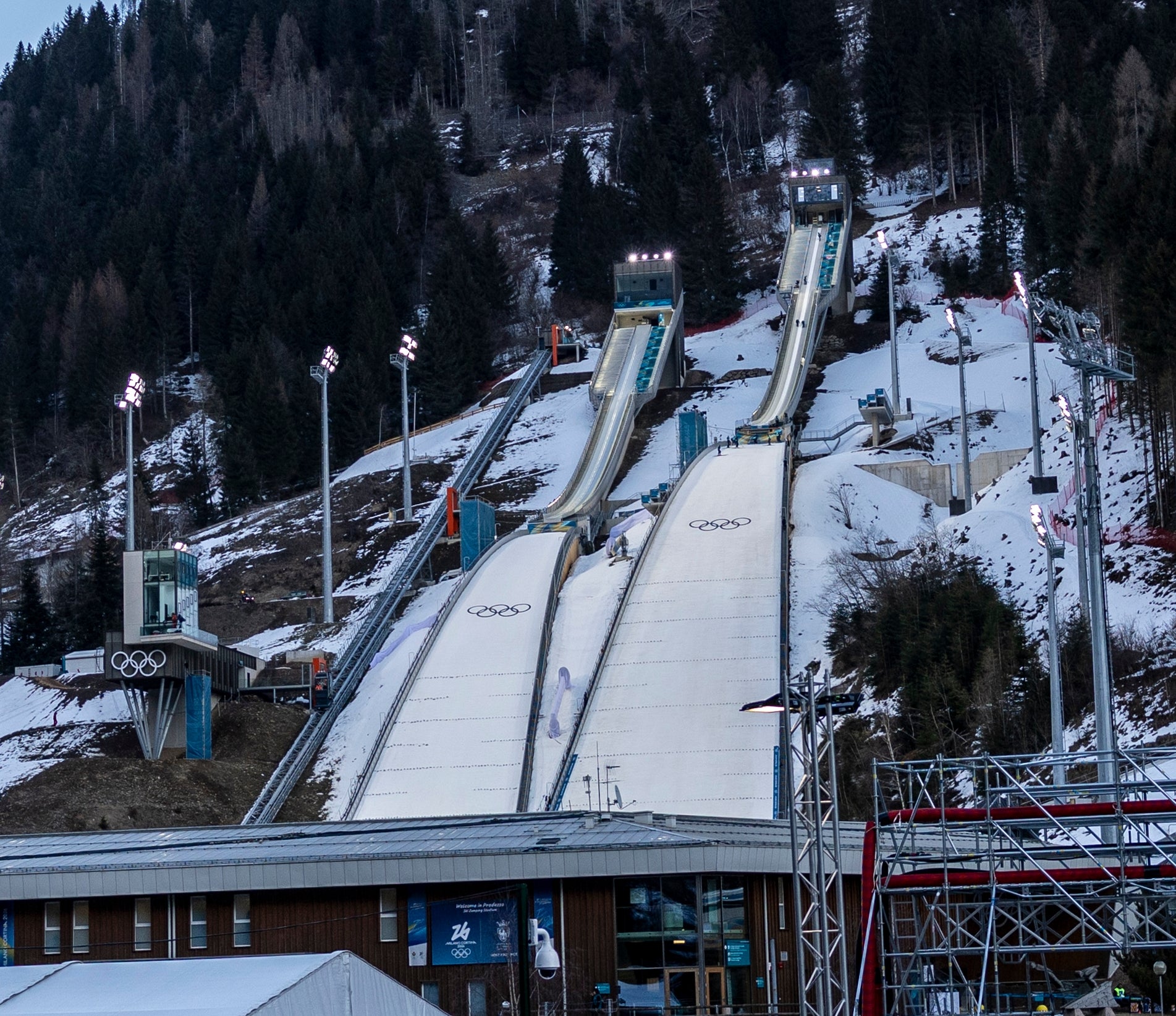 Hoppramper i et snødekt fjellområde med olympisk merkevare og folk som går i nærheten