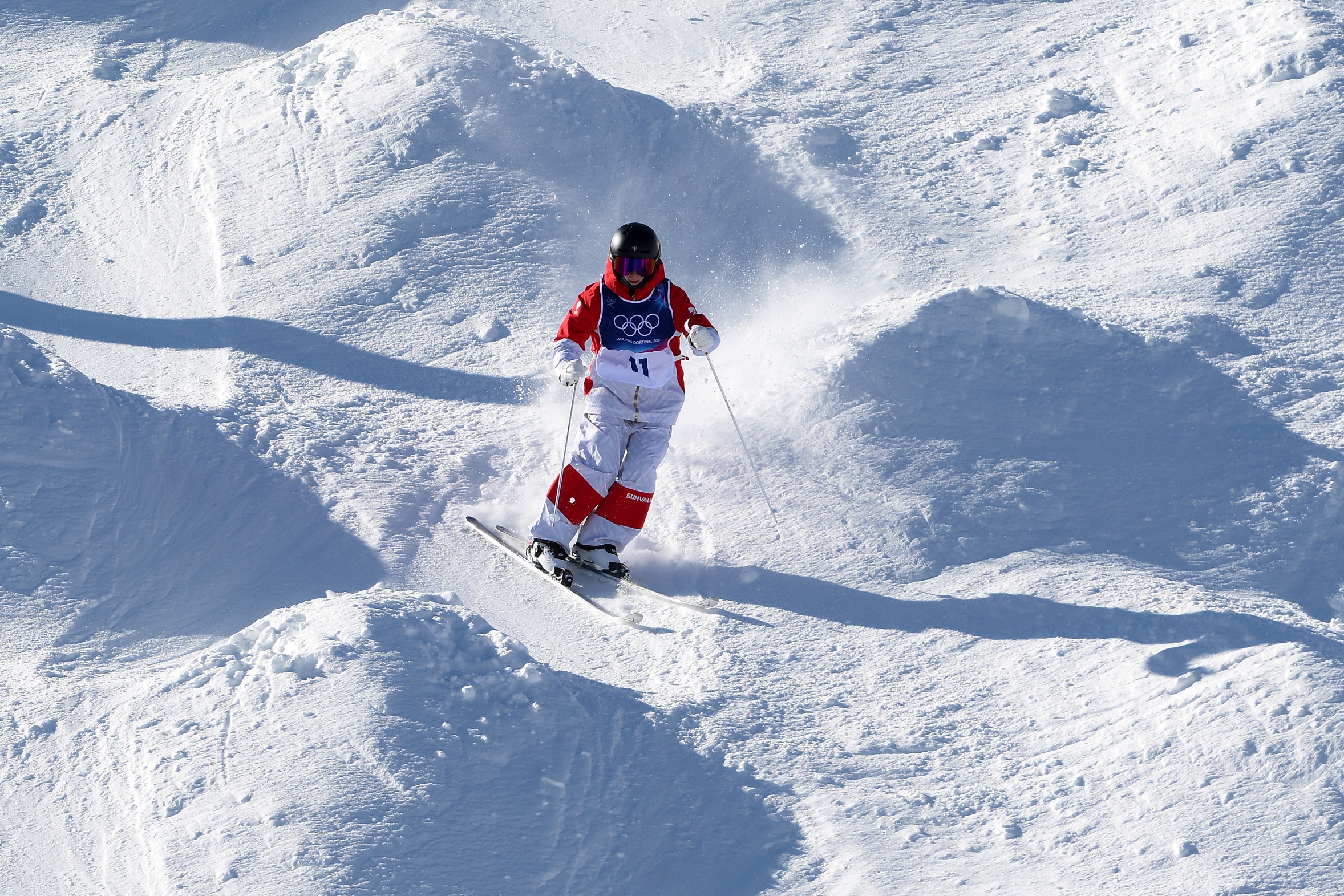 Person som går på ski ned en mogulbane iført en nummerert trøye og verneutstyr, og deltar i et konkurrerende skiarrangement