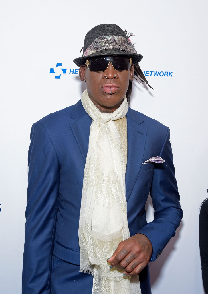 A idiosyncratic   successful  a stylish suit   with a scarf and chapeau  attends an event, wearing sunglasses and distinctive accessories