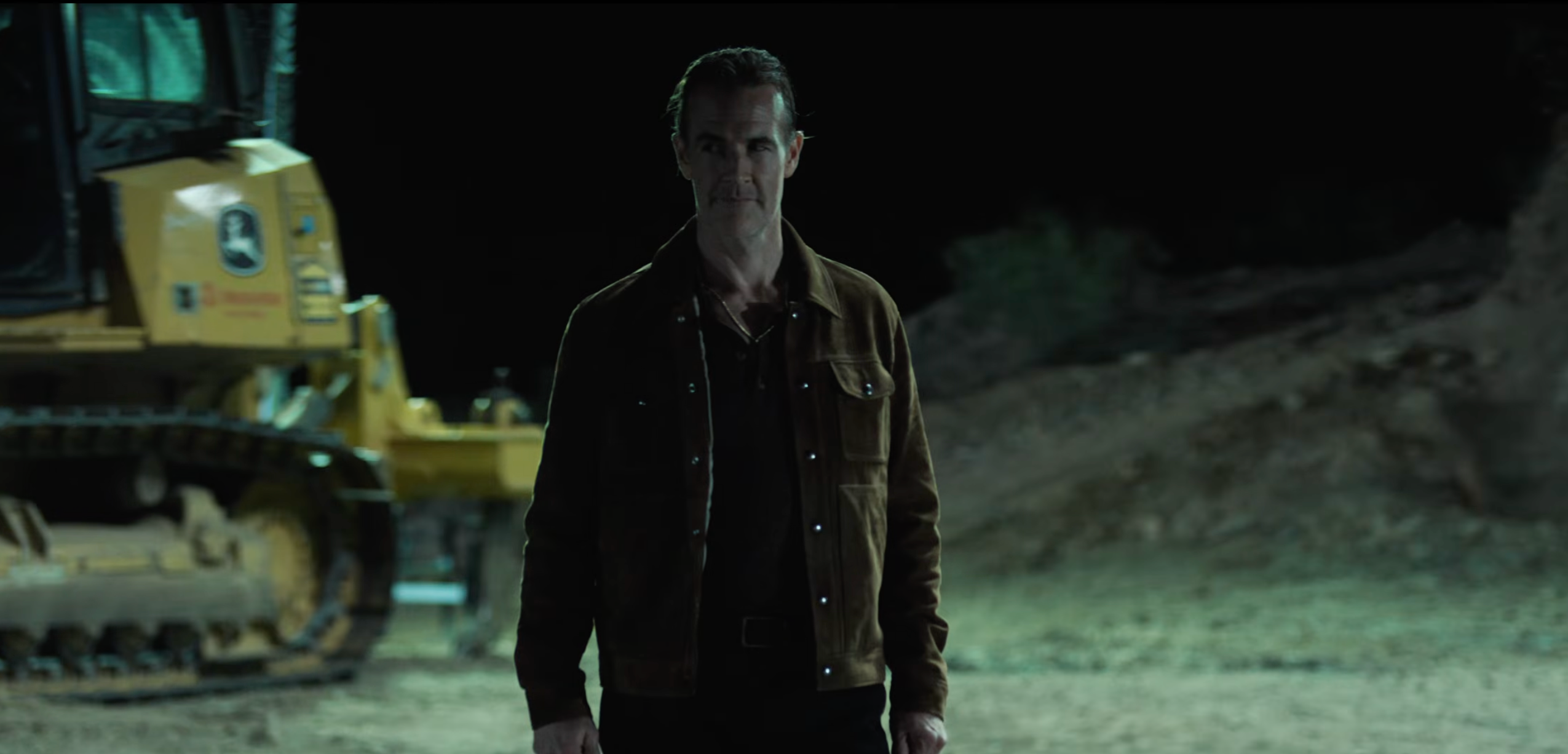 A idiosyncratic   stands successful  beforehand   of operation  instrumentality  astatine  night, wearing a acheronian  jacket. The mounting  suggests a country   from a TV oregon  movie   production