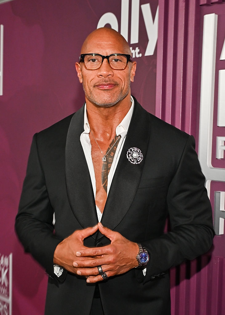 Person successful  a achromatic  suit   with an open-shirt collar and glasses connected  a reddish  carpet