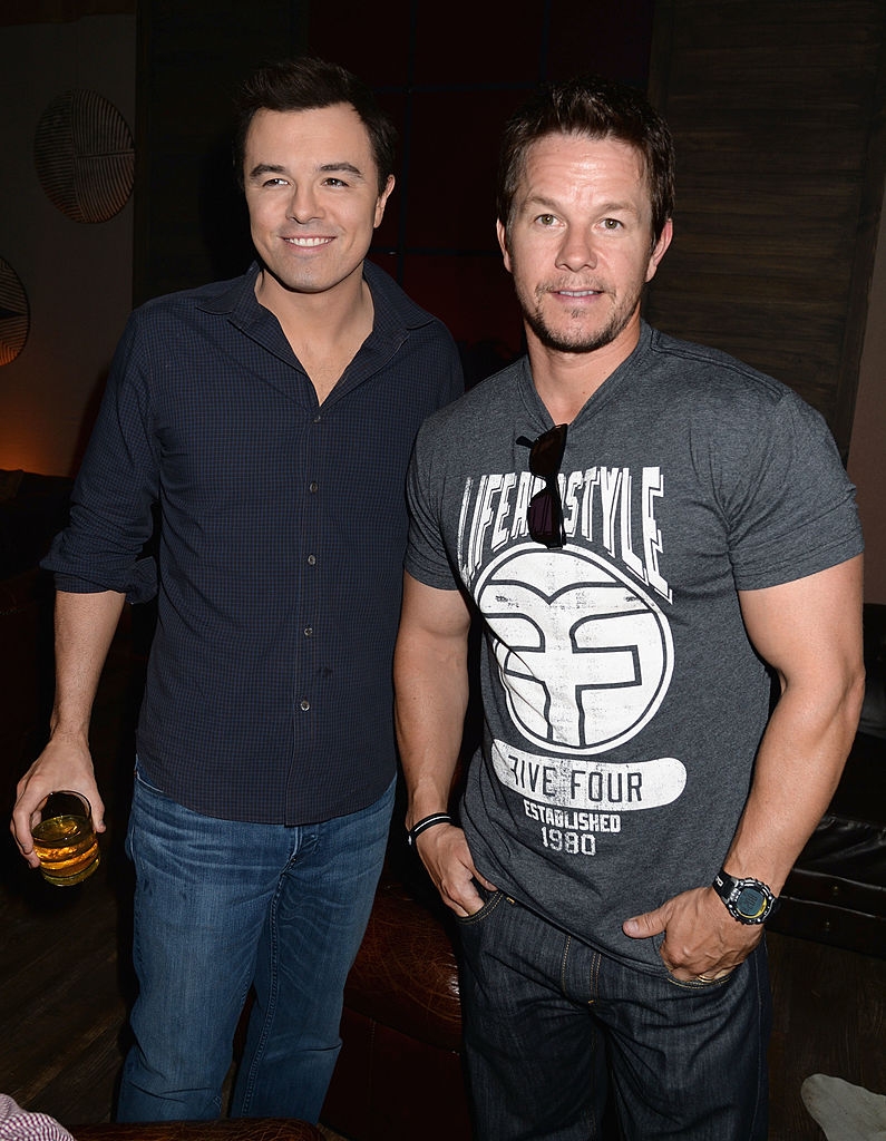 Two men are posing together; 1  successful  a casual button-up garment  and jeans, the different   successful  a graphic t-shirt