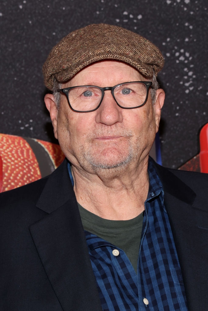 A idiosyncratic   wearing a level  cap, glasses, a blazer, and a checkered garment  appears astatine  an event