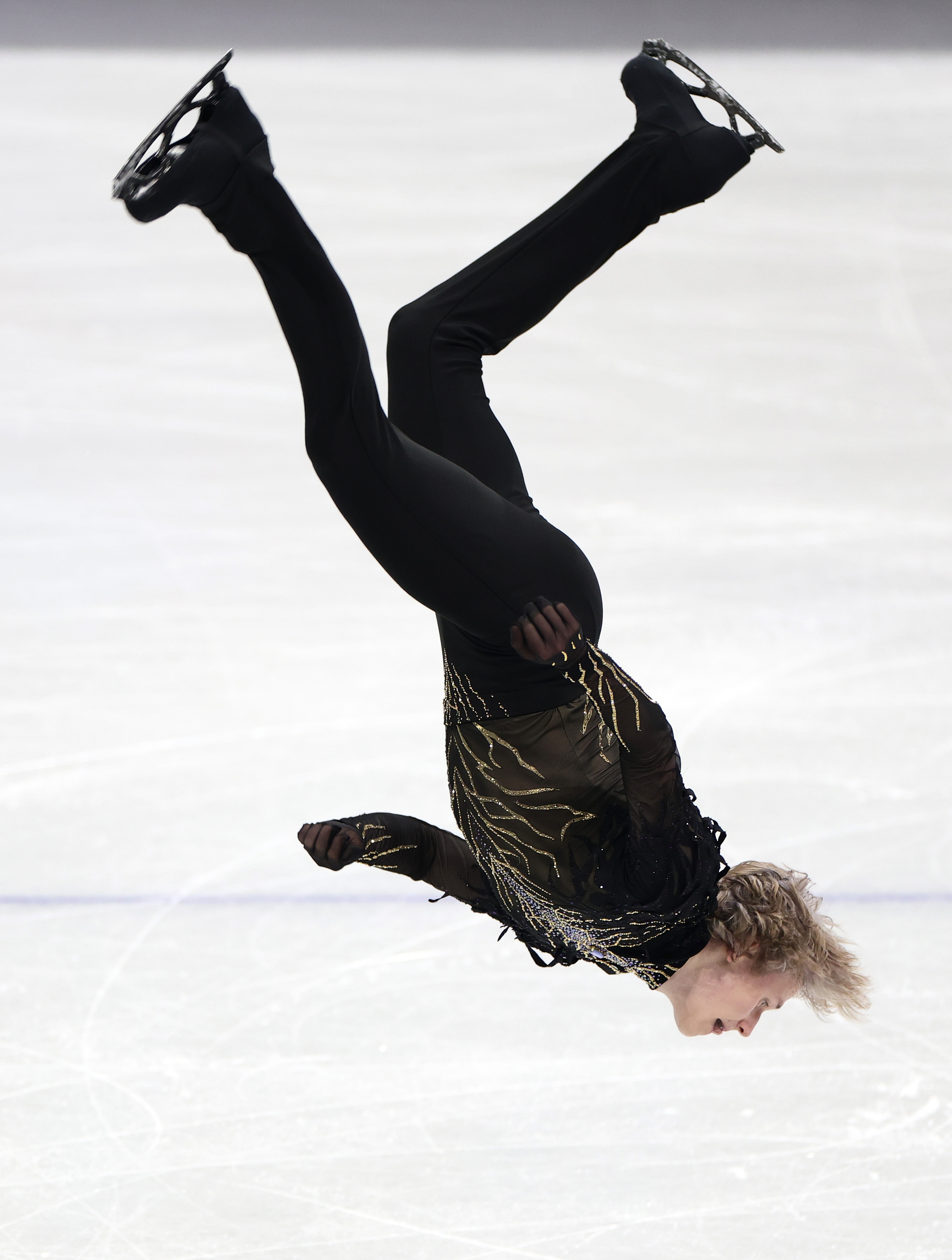 Kunstløper utfører et spinn i luften på skøytebanen, iført et intrikat mønstret antrekk