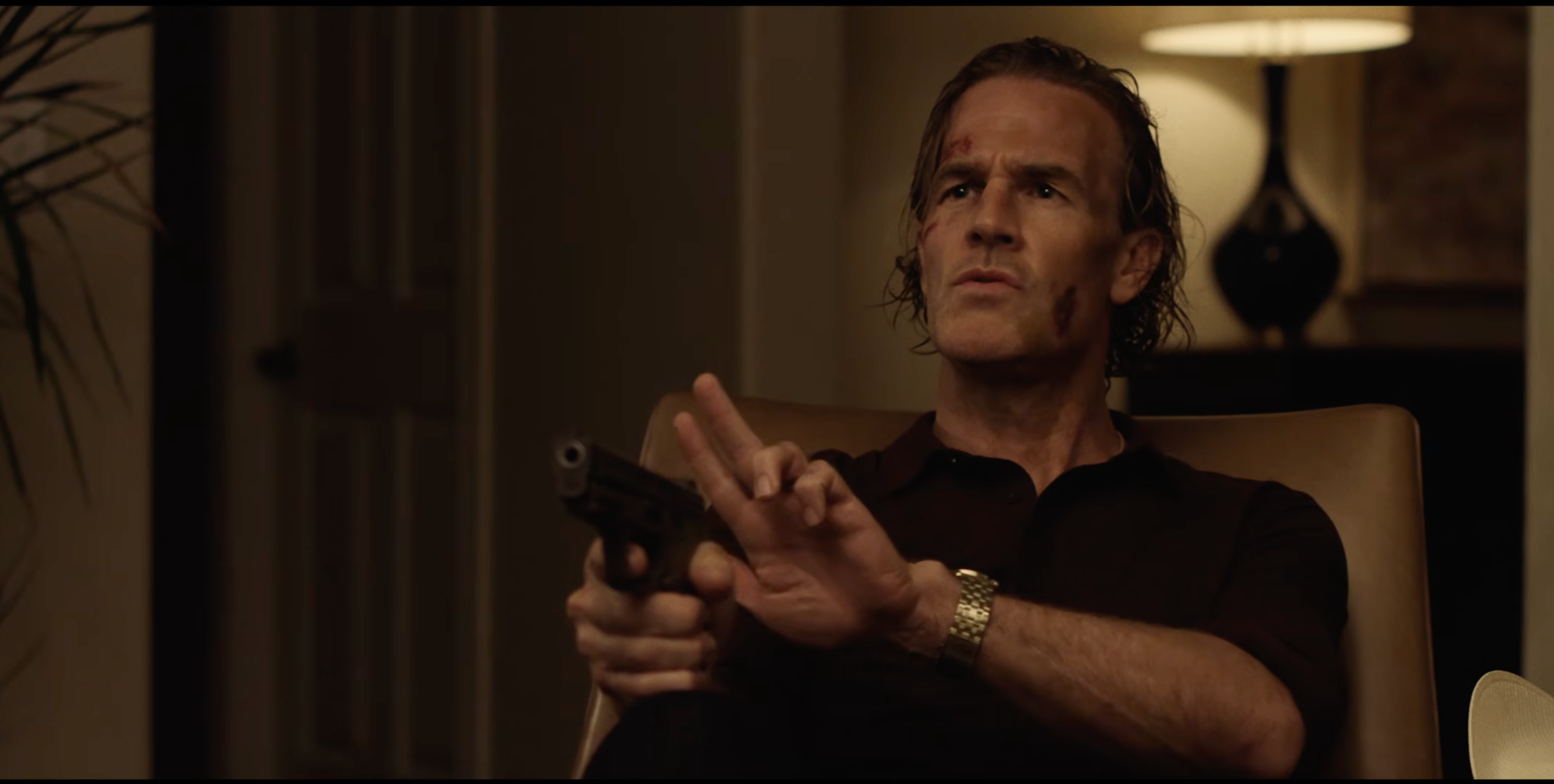 Person successful  armchair holding handgun, looking serious, with insignificant  facial injuries, successful  a dimly lit room