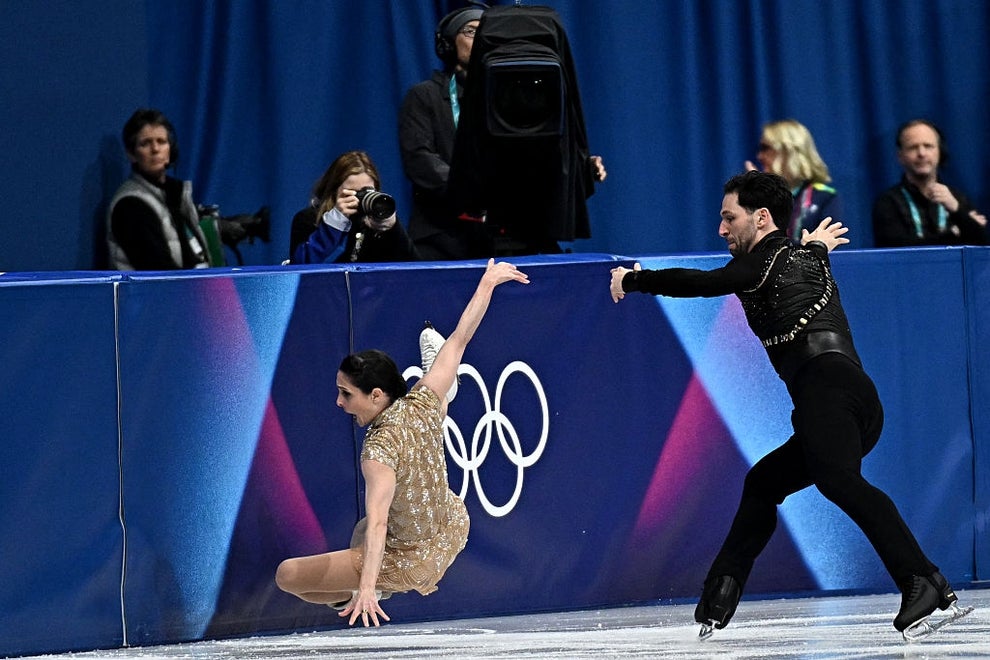 Figure skaters perform dynamic routine on ice; the female skater wears a sparkly dress while the male skater wears a sharp, black outfit