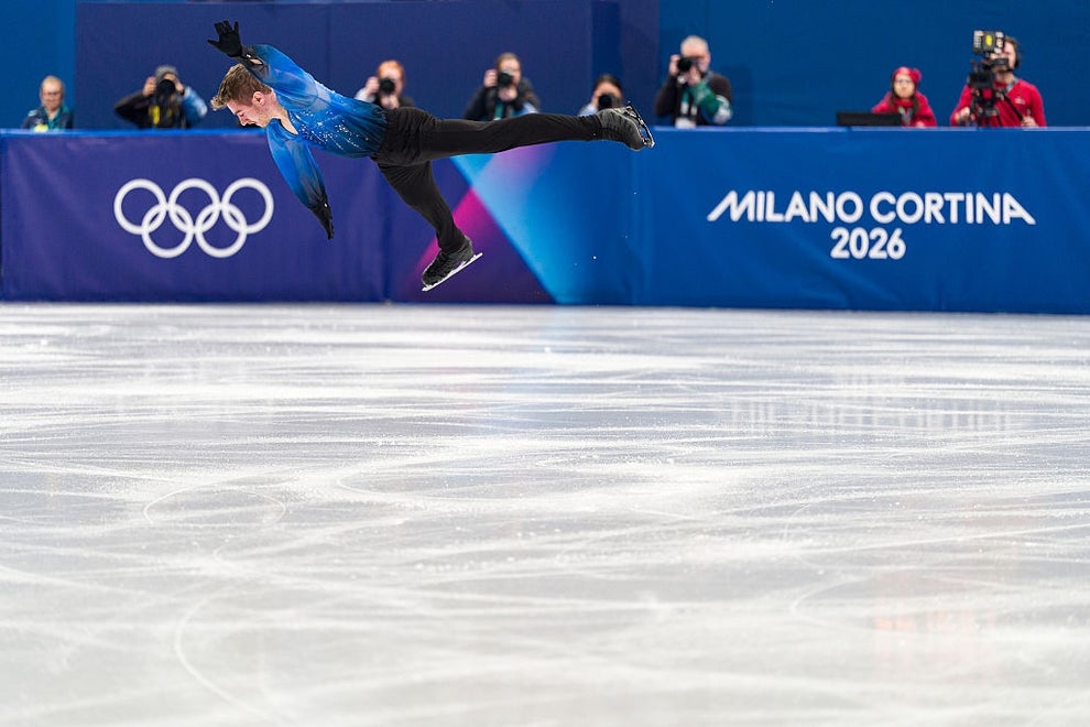 Figure skater performs a jump at Milano Cortina 2026 event; Olympic rings and event logo in the background