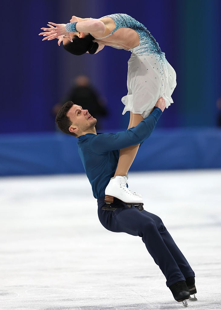 Figure skaters perform a dramatic lift on the ice, with the woman gracefully poised above the man