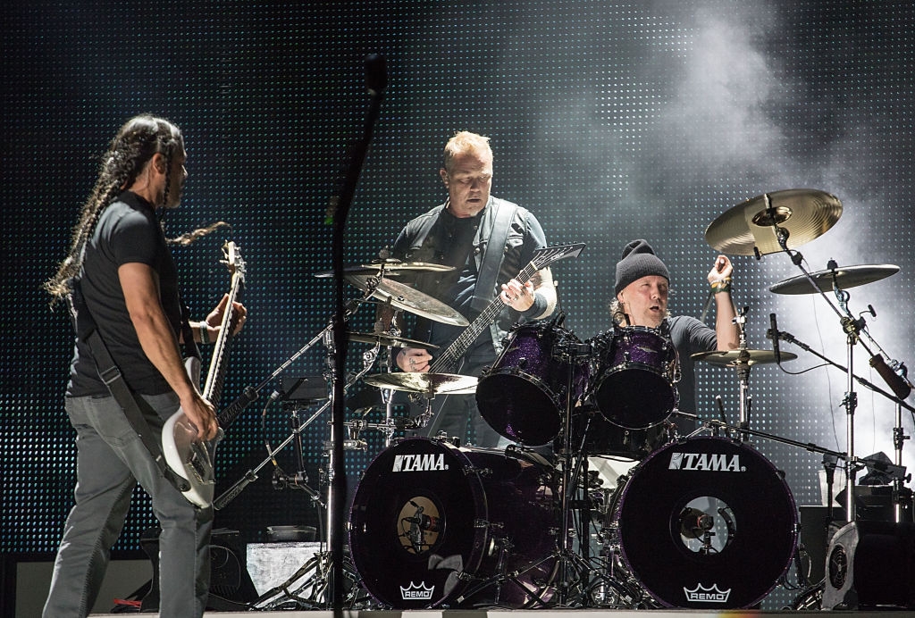 Three musicians execute  energetically connected  signifier    with guitars and drums, surrounded by signifier    lights and fume  effects