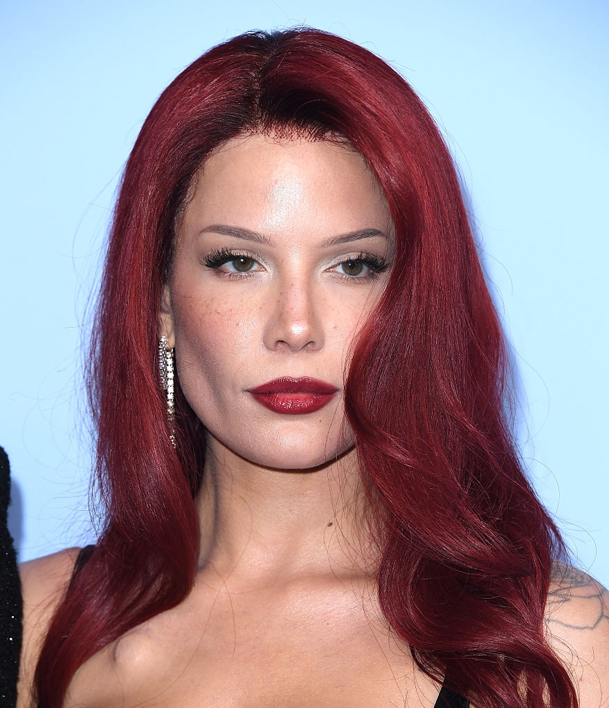 A idiosyncratic   with long, wavy hairsbreadth  poses confidently astatine  an event, wearing a sleek outfit and elegant earrings