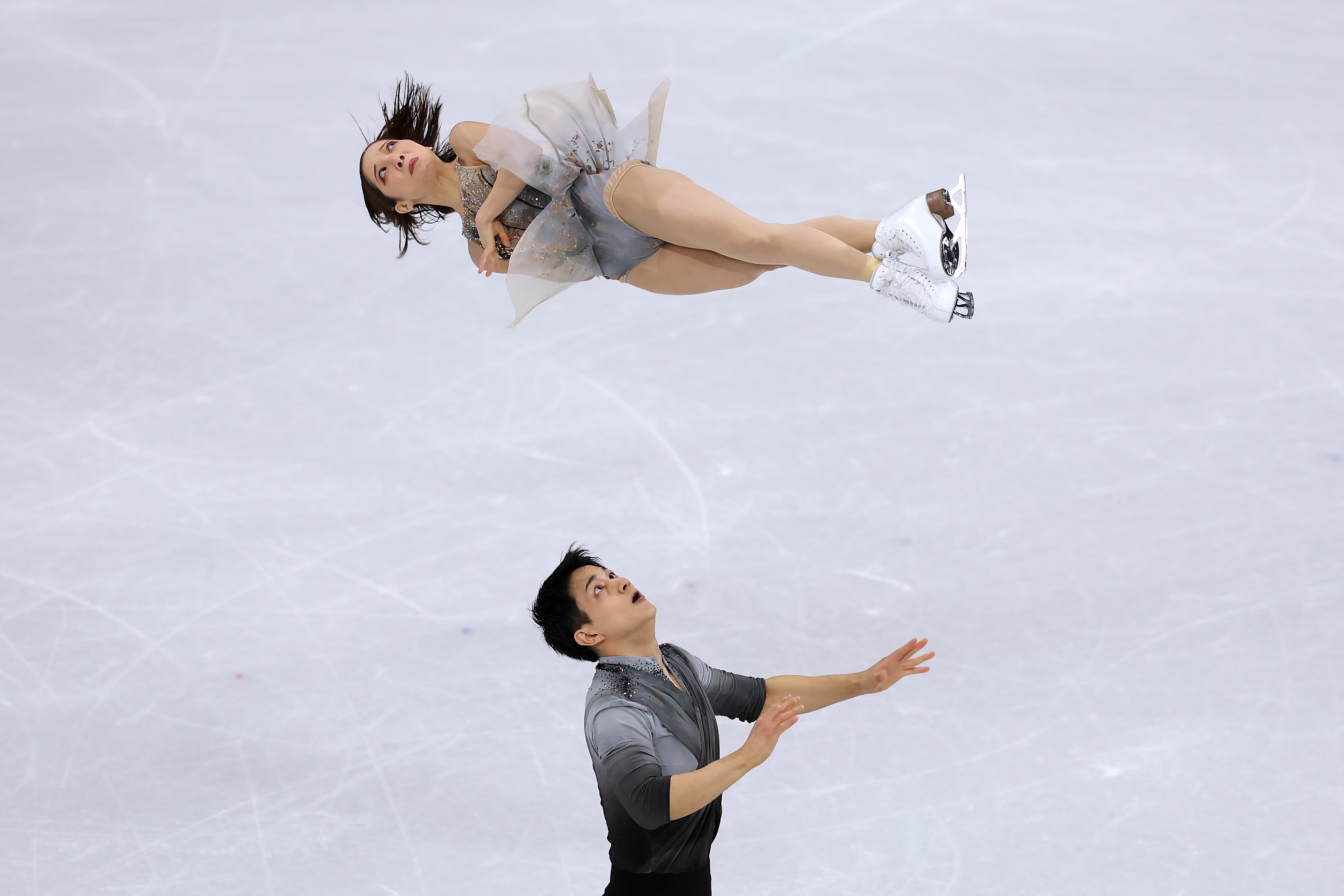 To kunstløpere utfører et løft, med kvinnen i luften og mannen støttende nedenfra på skøytebanen