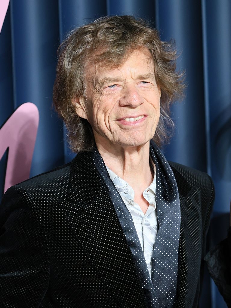 A idiosyncratic   with agelong  hairsbreadth  smiles portion    wearing a acheronian  suit   with a textured garment  astatine  a ceremonial  event