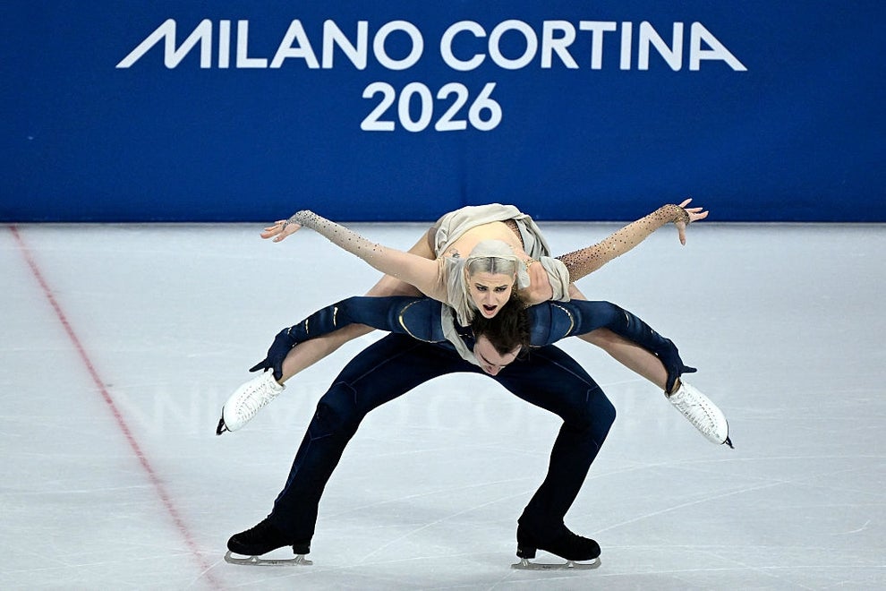 Figure skating pair performing an intricate lift at the Milano Cortina 2026 event, with the sign visible in the background