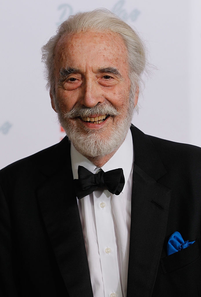 Elderly antheral   with achromatic  hairsbreadth  and beard wearing a achromatic  tuxedo, bow tie, and a bluish  pouch  square, smiling astatine  an event