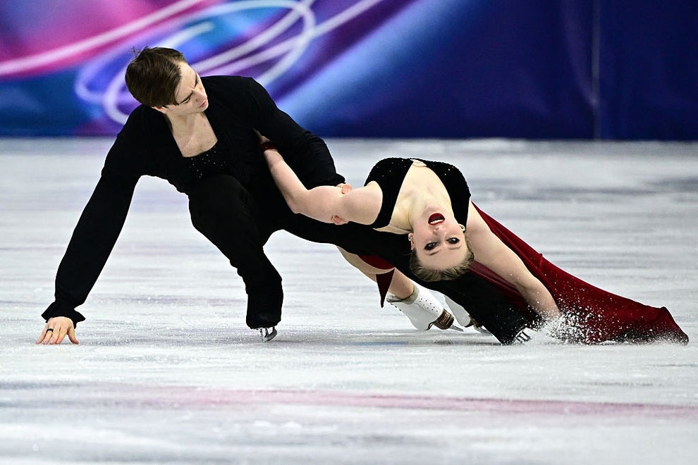Figure skaters perform an intricate move on the ice; one skater leans back dramatically while the other supports. Elegant display of athleticism and grace