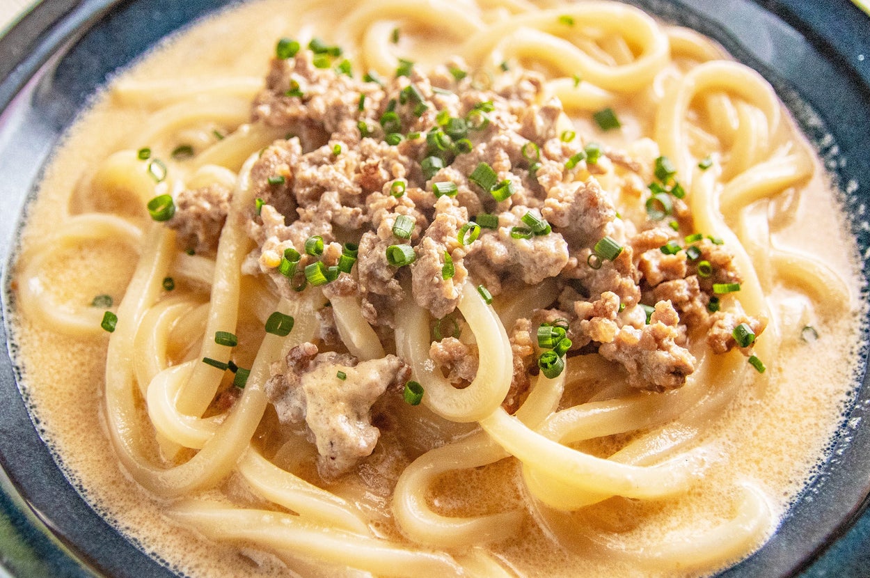 器に盛られた肉とネギがトッピングされたクリーミーなスープうどん。