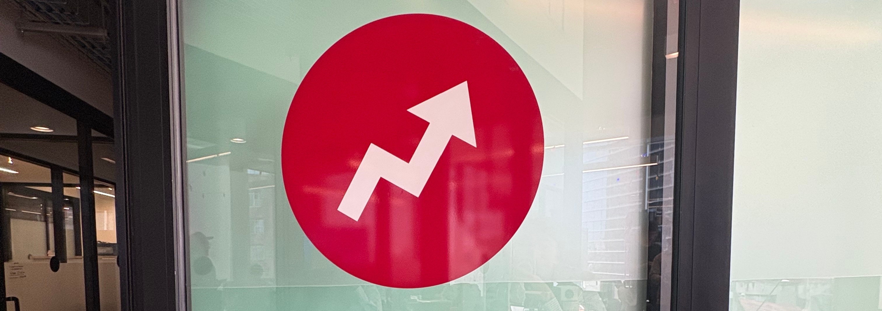 Logotipo circular con una flecha ascendente en una puerta de oficina de vidrio. Muestra movimiento o crecimiento