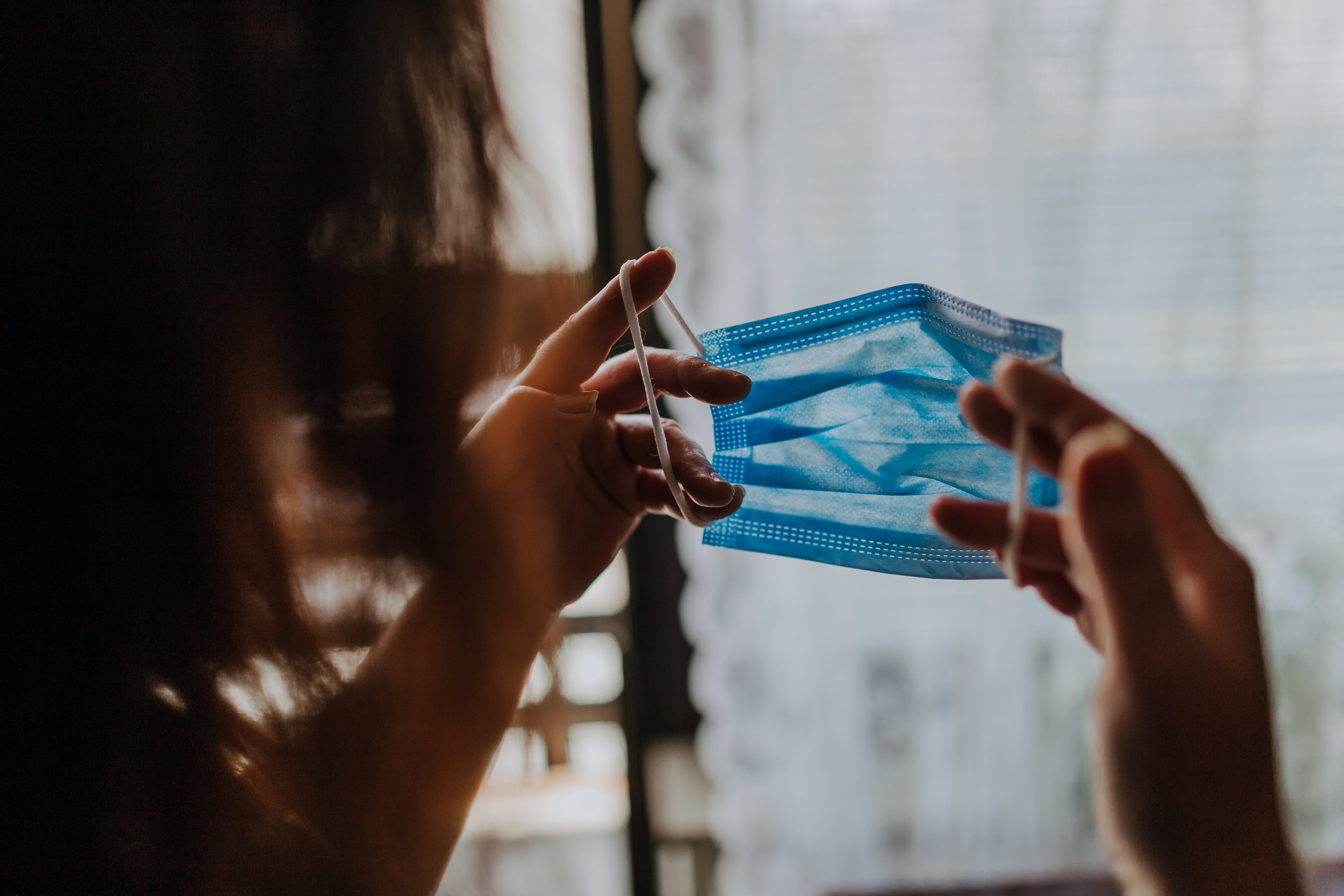 Person holding a blue surgical mask by the ear loops, preparing to wear it indoors