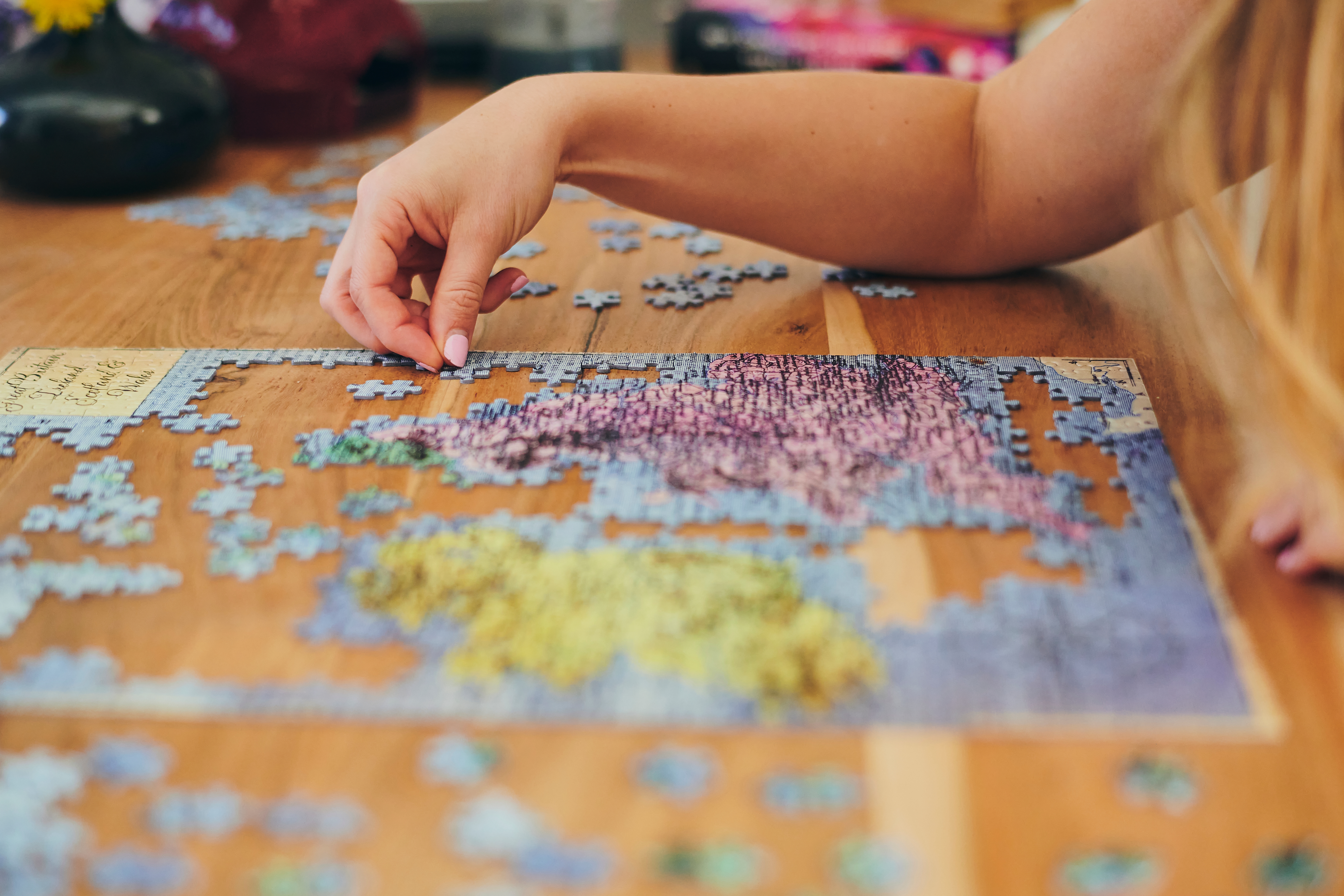 Person assembling a puzzle on a wooden table, with visible sections completed