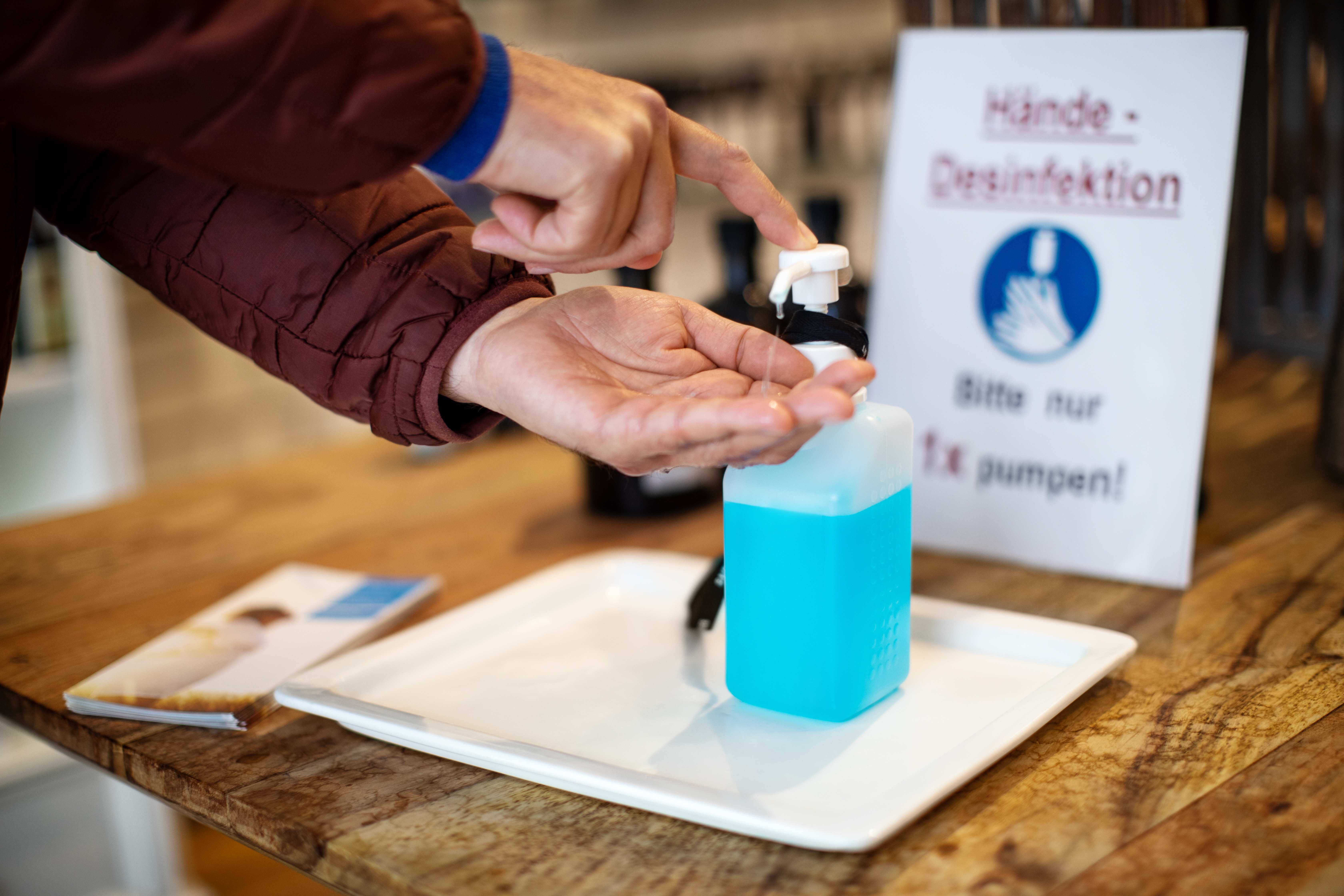 Person using hand sanitizer from a pump bottle, with a sign advising limited usage nearby