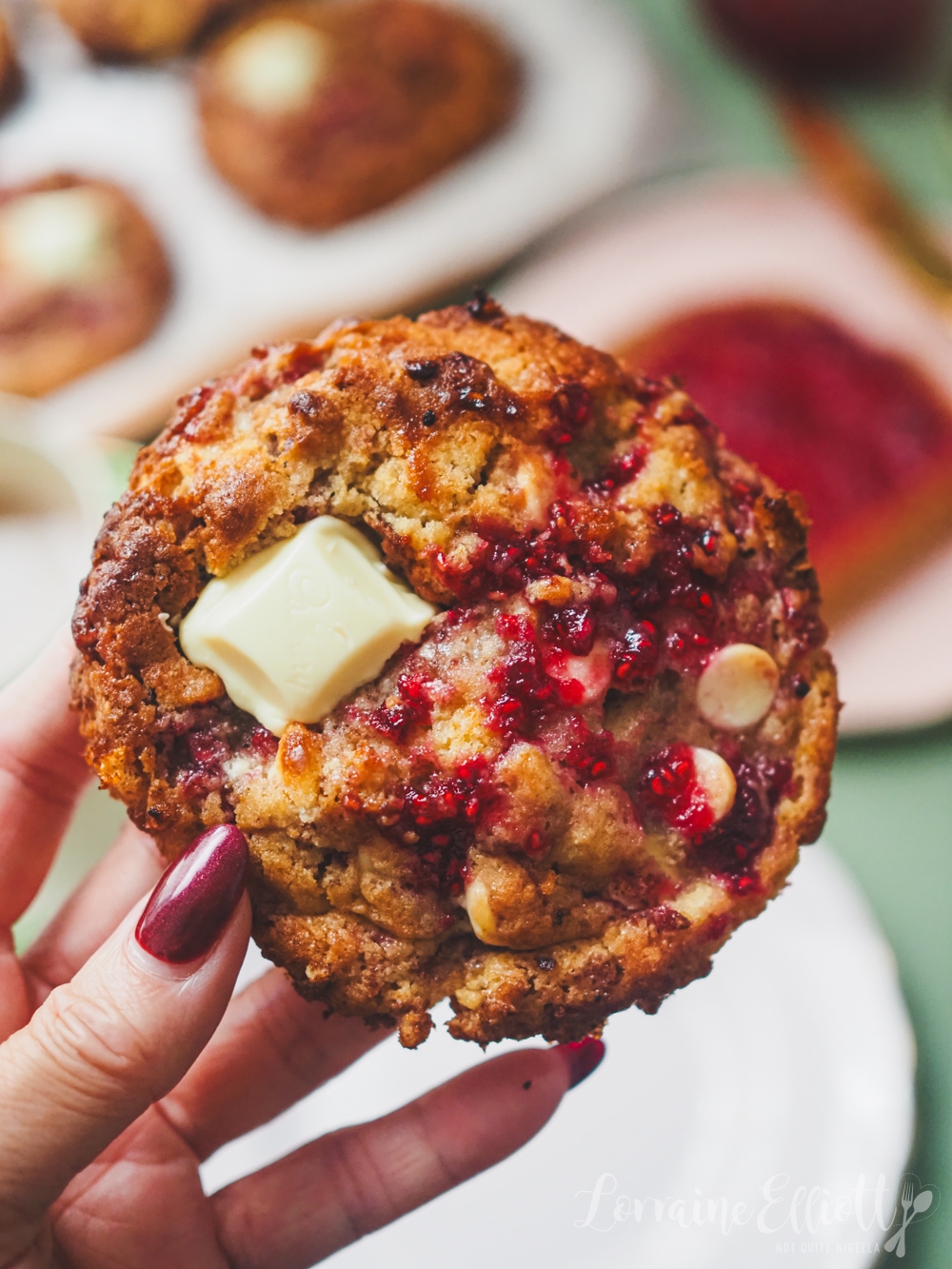 A manus holds a raspberry cooky with achromatic cocoa chunks. A sheet with much cookies is blurred successful the background