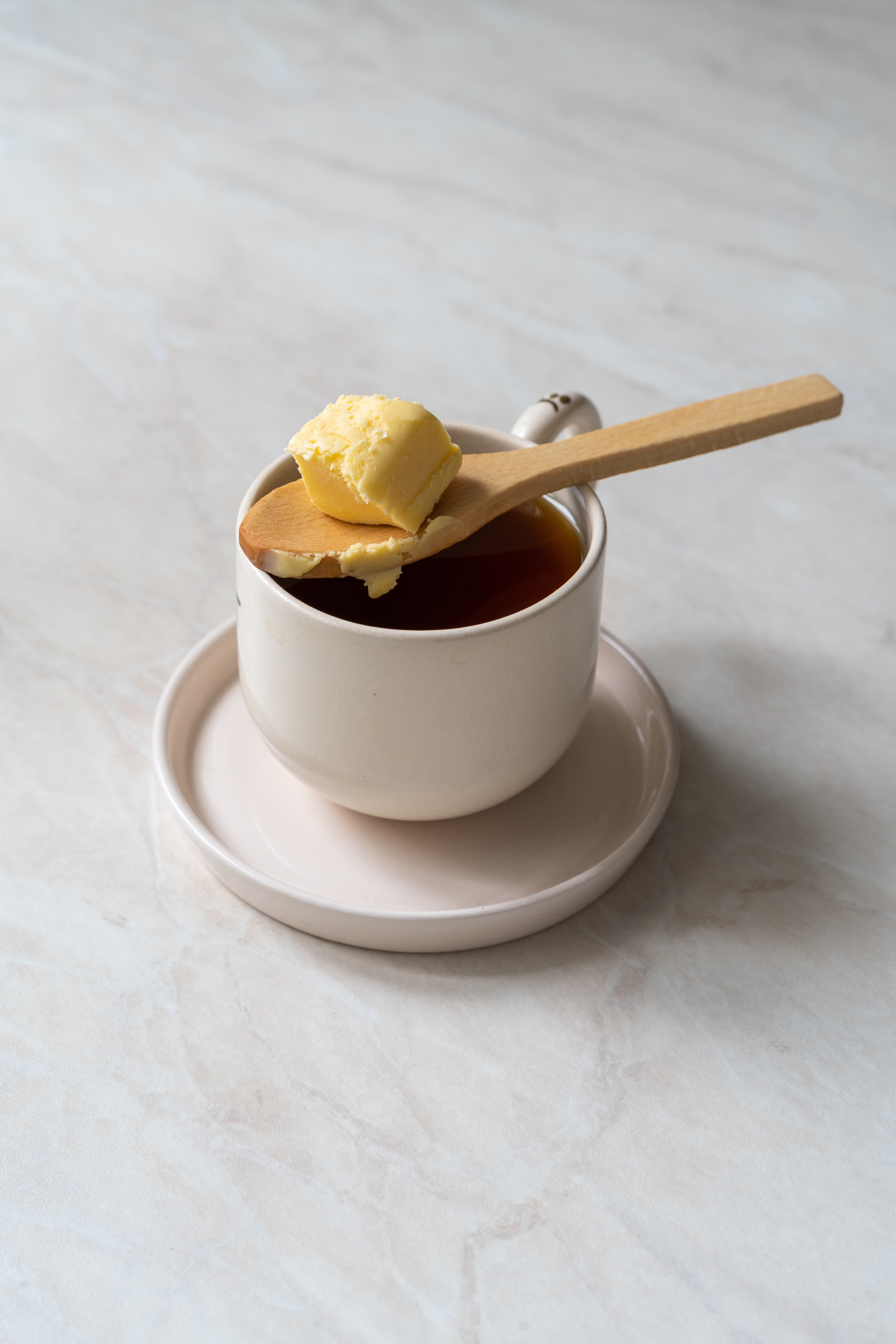 A hot cup of tea with a wooden spoon resting on top, holding a pat of butter above the cup